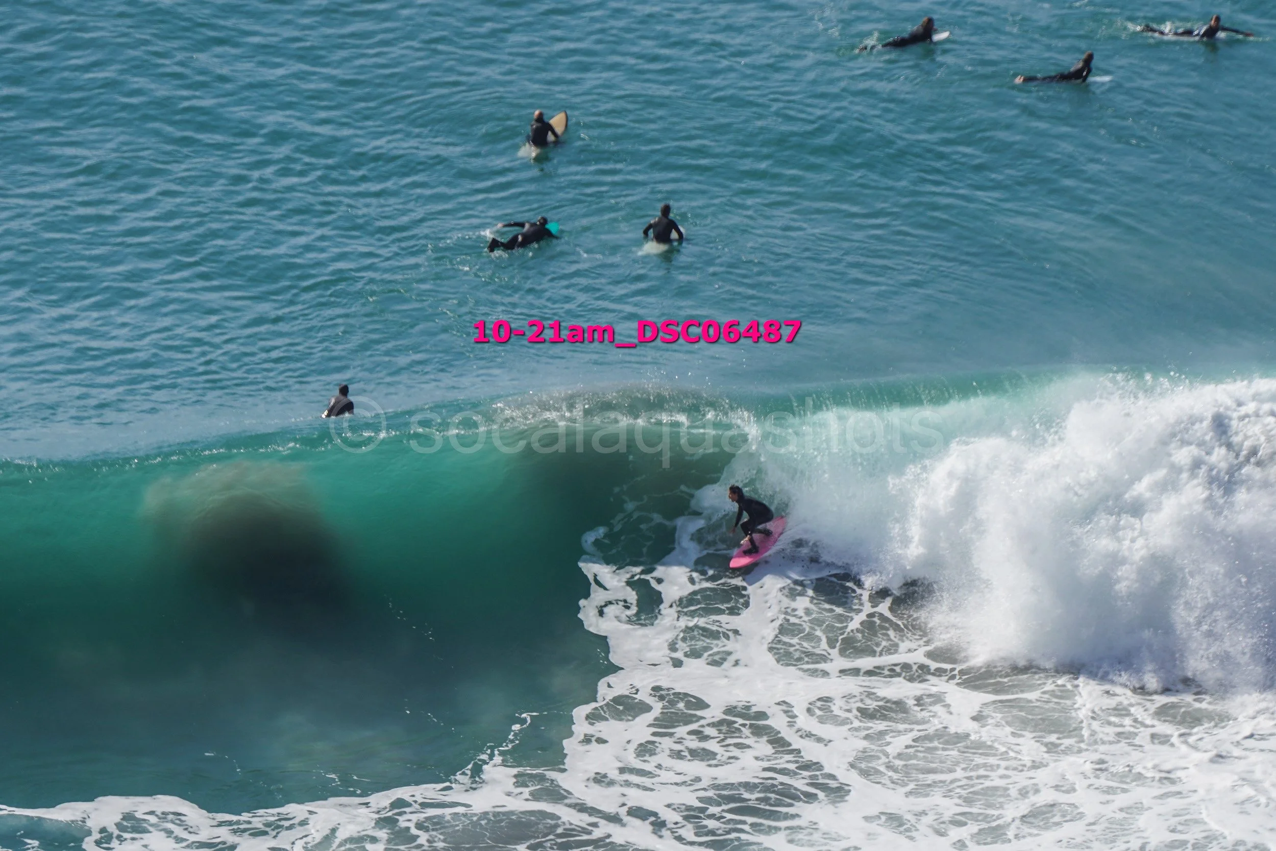Surfer riding a wave with several people swimming and surfing in the background.