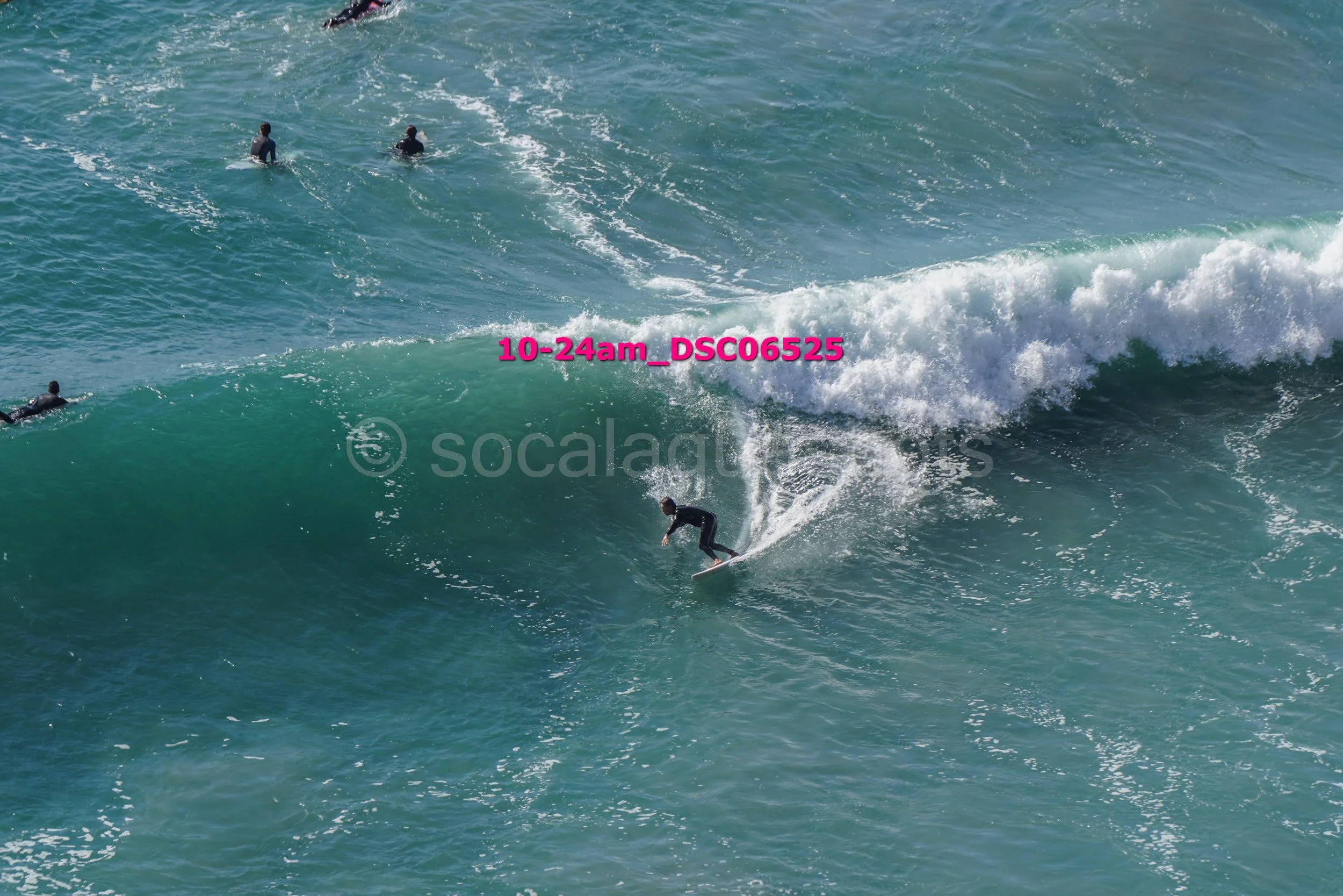 A person surfing on a large wave in the ocean with several other surfers in the background.