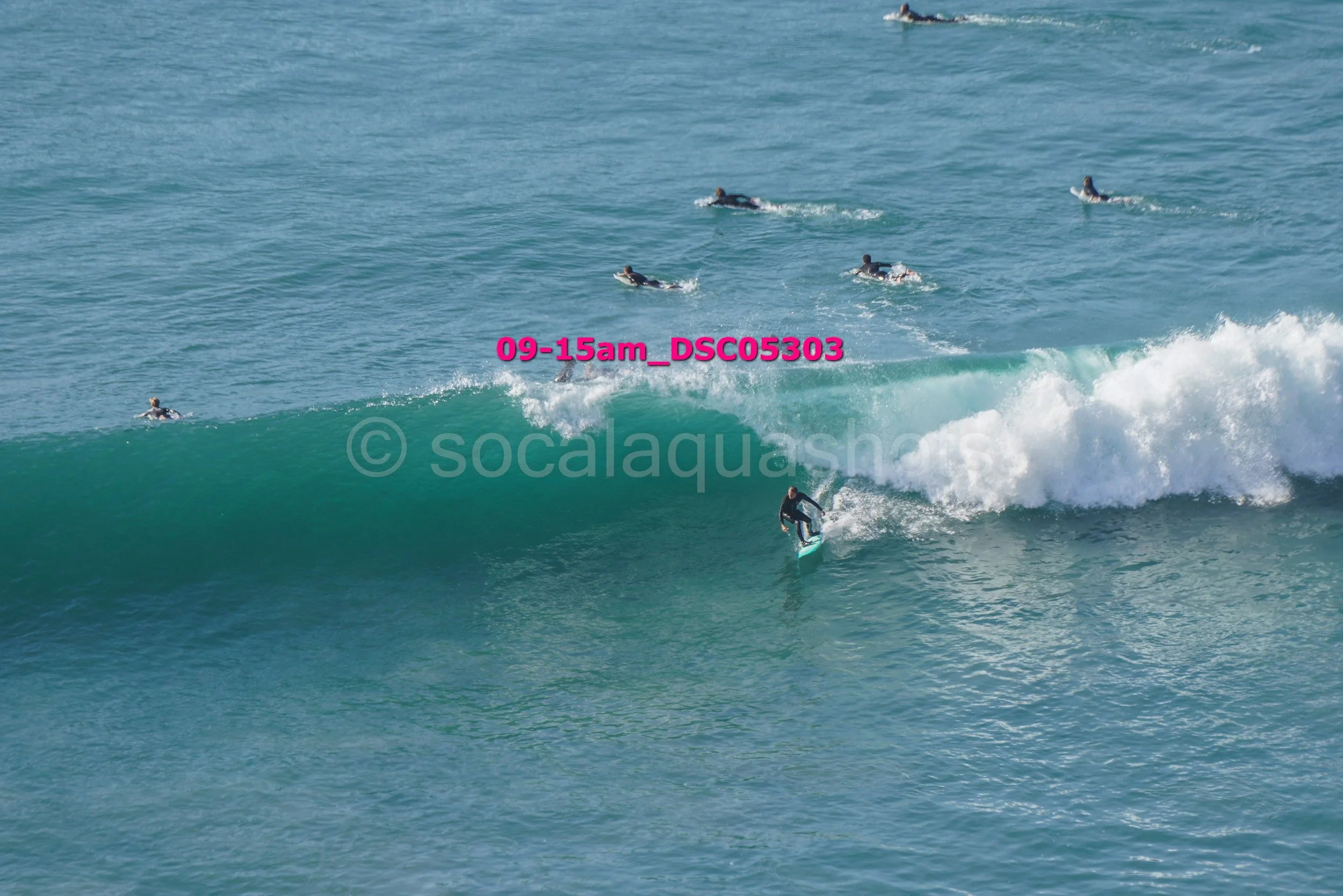 Surfer riding a wave with several other people swimming in the ocean nearby.