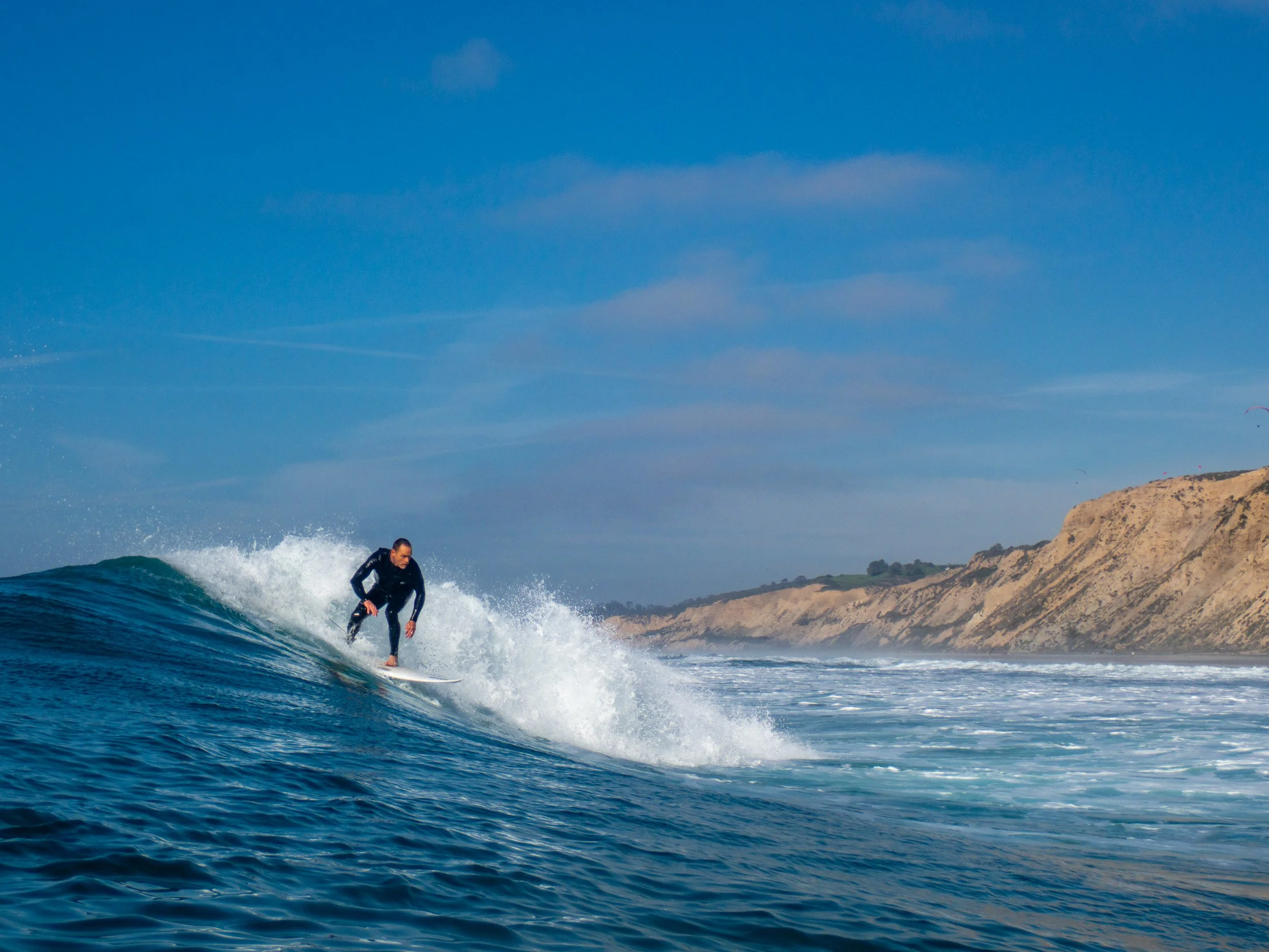 A person wearing a wetsuit surfing on a wave in the ocean near a coastal land with cliffs.
