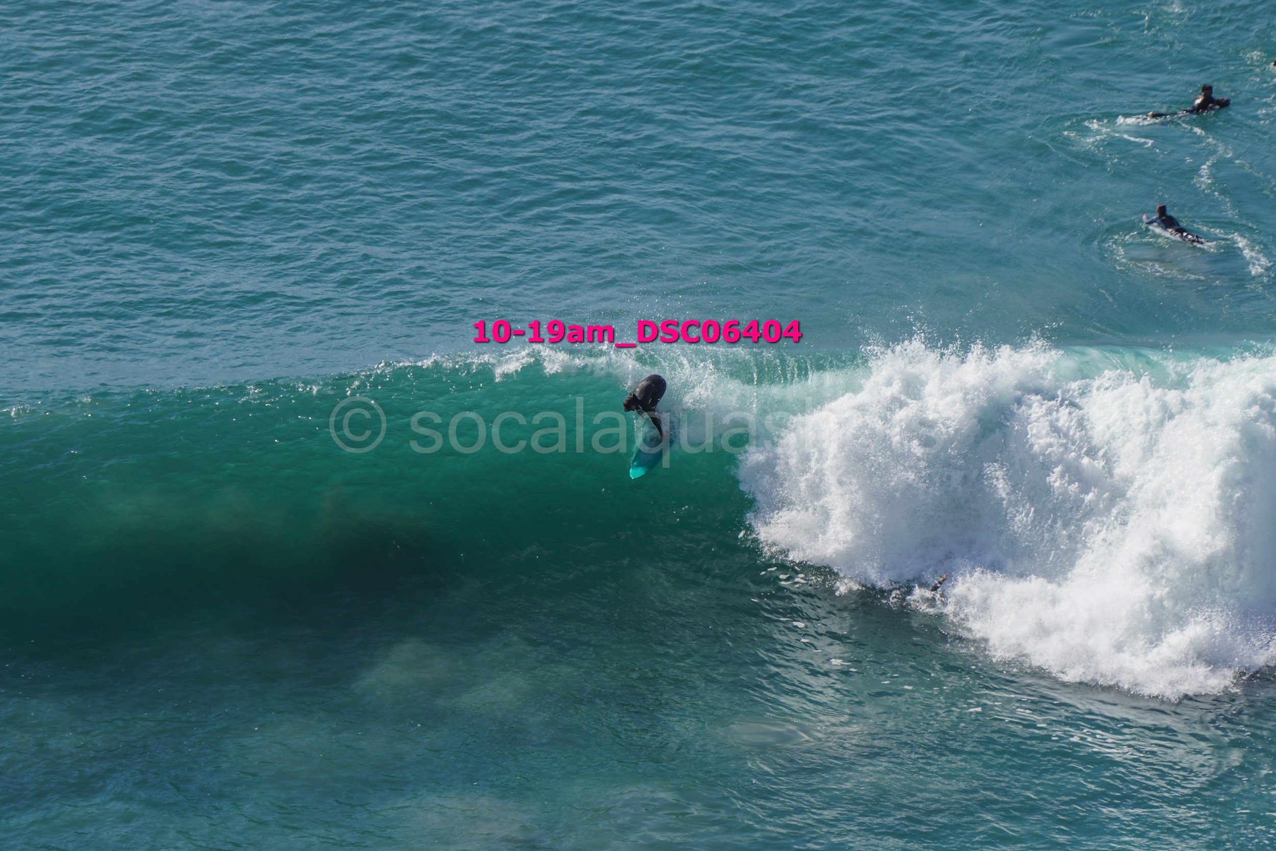 Surfer falling off a wave at the ocean, with two other surfers in the background.