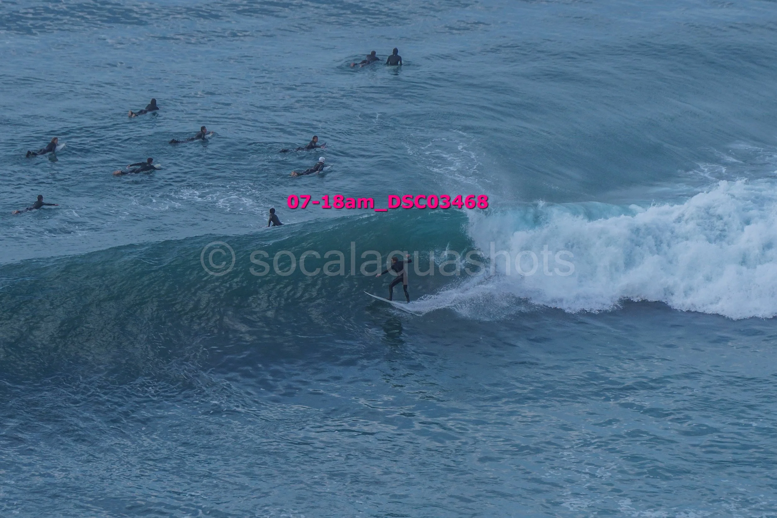A person surfing on a large wave with several other surfers in the water in the background.