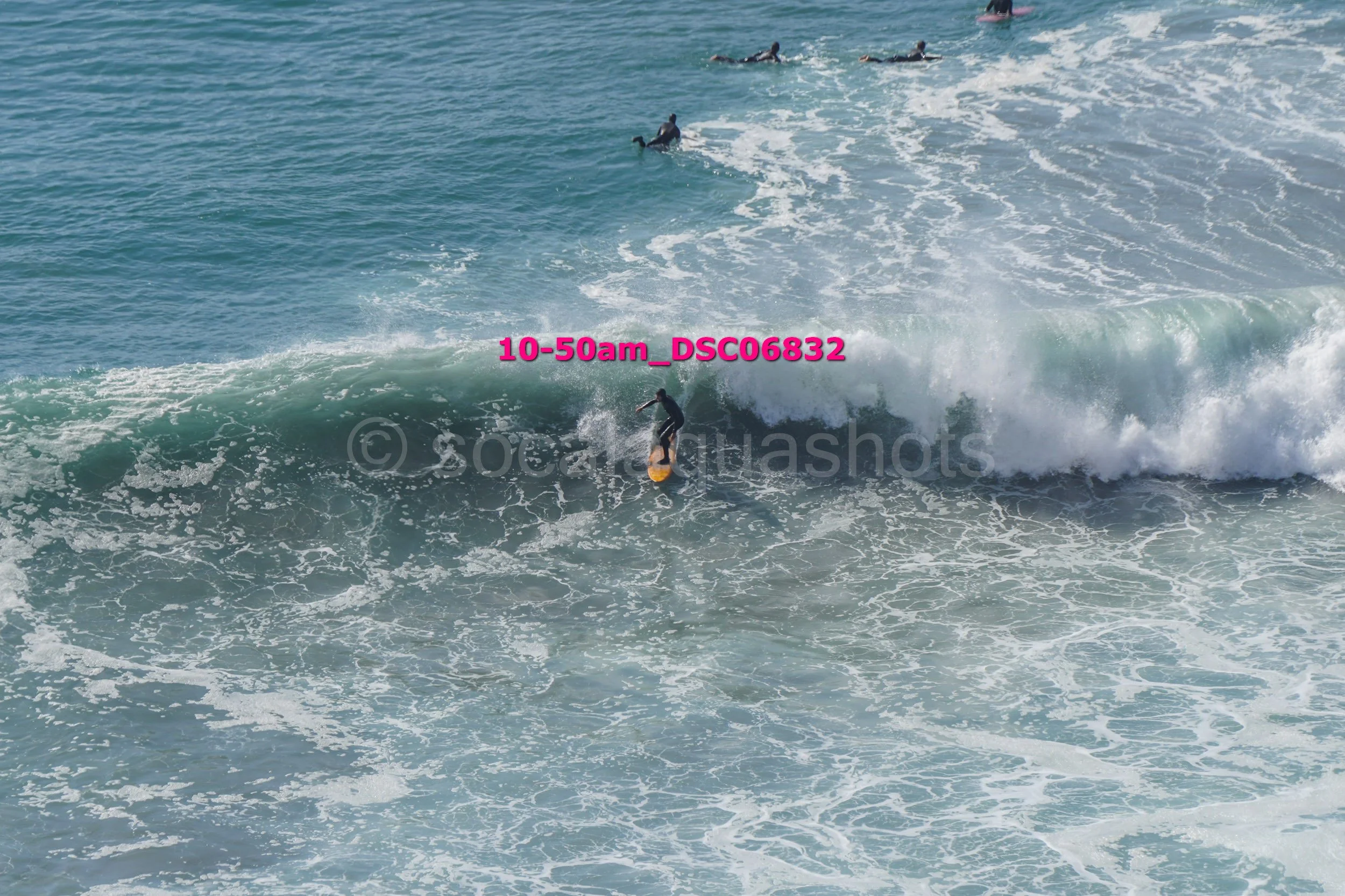 Surfer riding a wave in the ocean with several other surfers in the background.