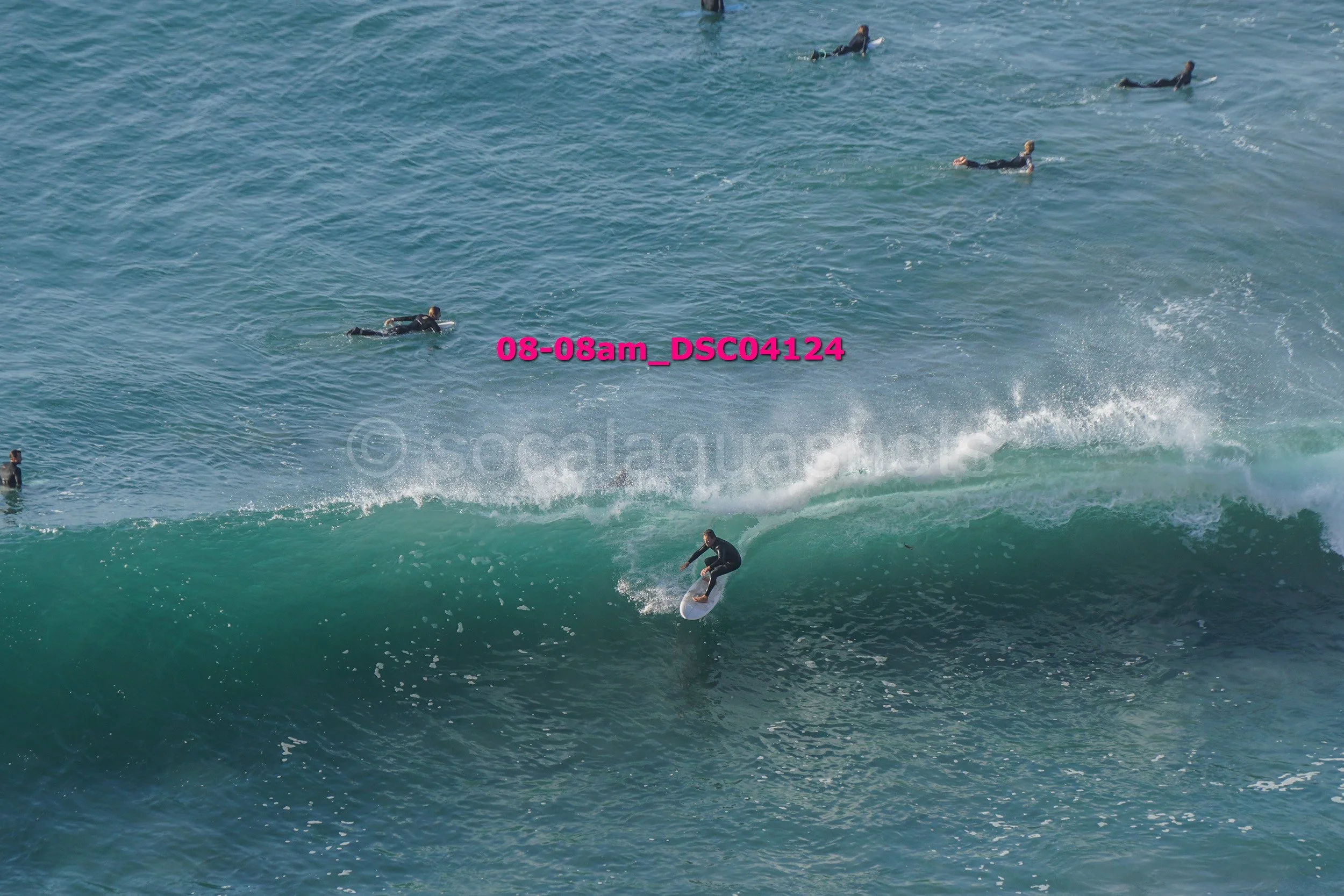 A person surfing on a wave with several other surfers in the water nearby.