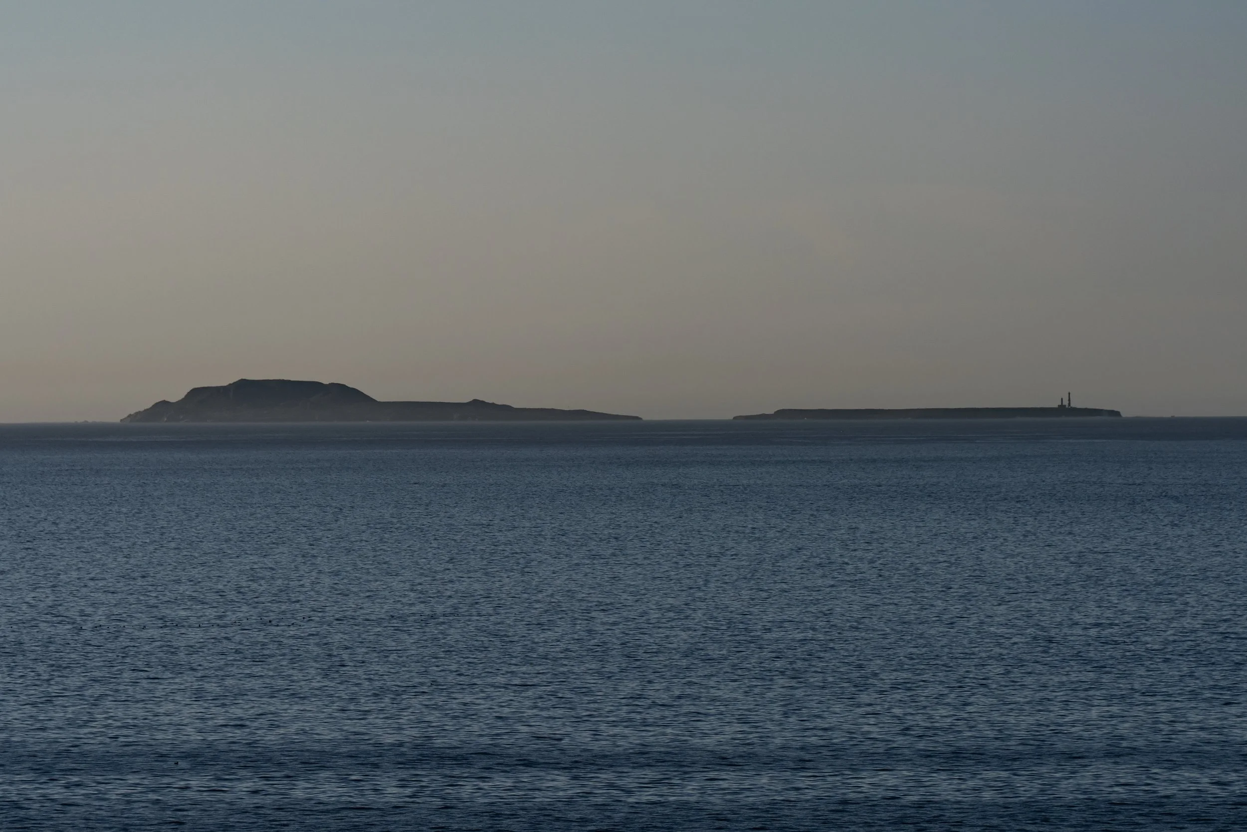 Ocean with two distant islands, one with a lighthouse on the right island.