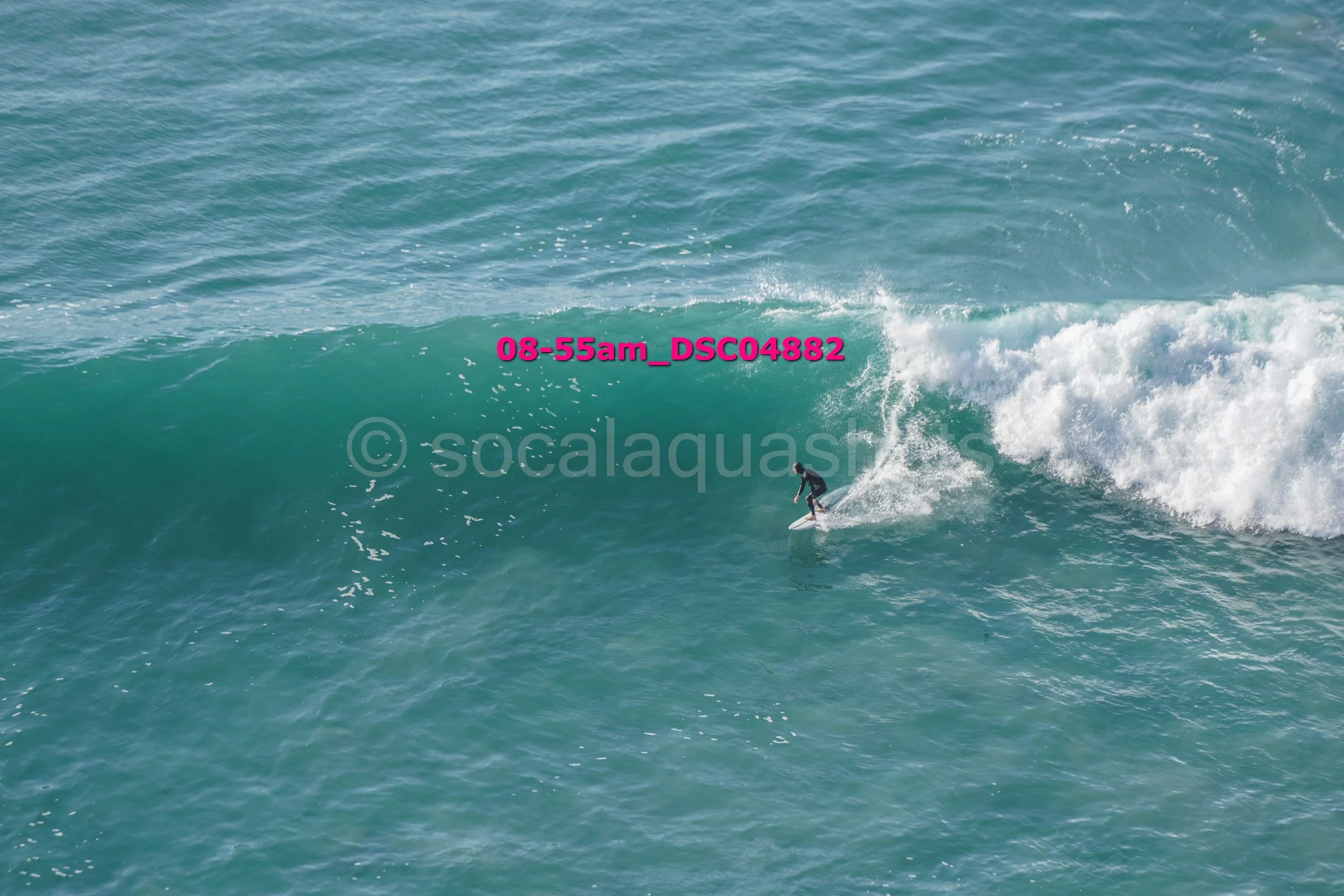 A surfer riding a large ocean wave with a clear blue sky.