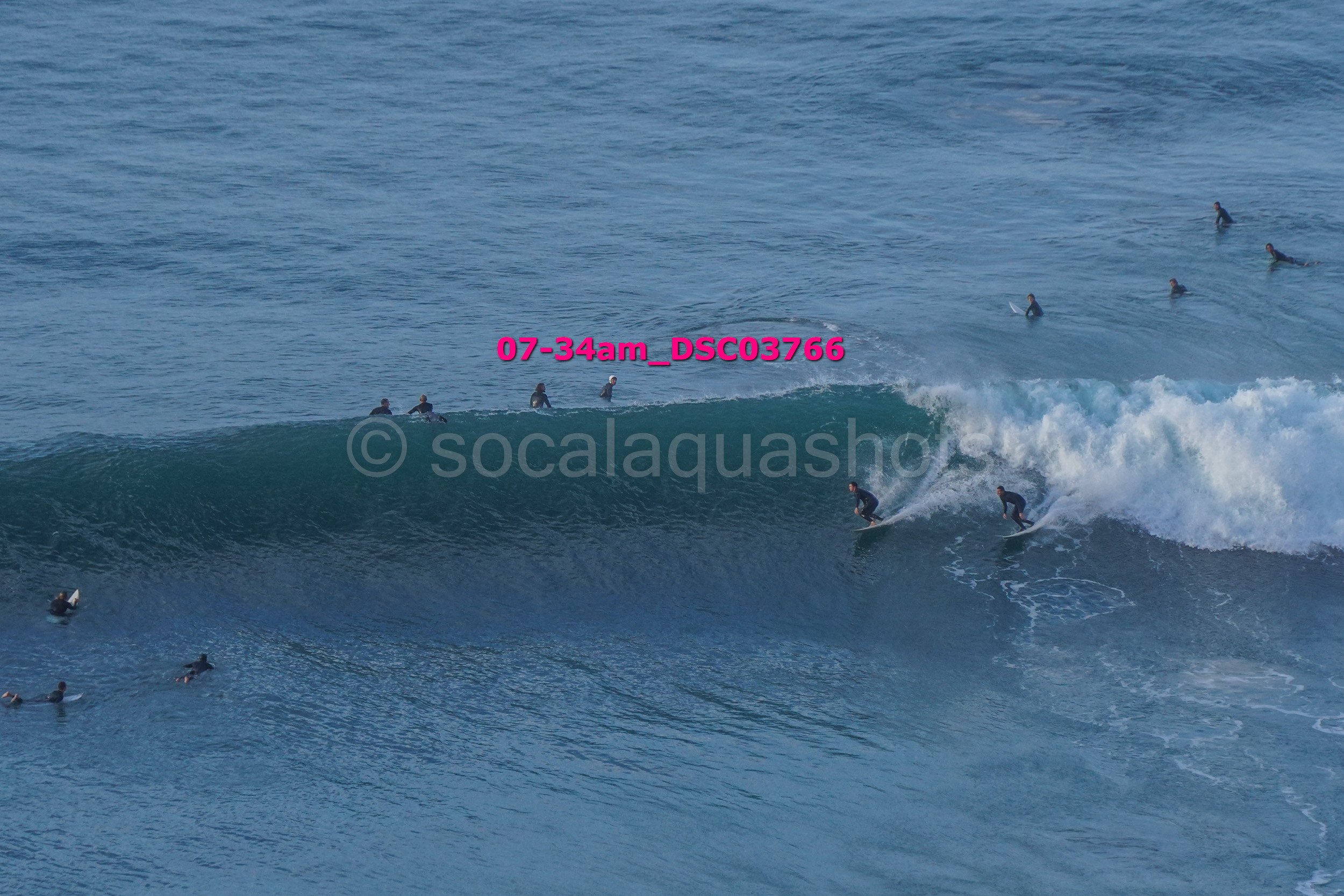 Multiple surfers in wetsuits riding and waiting for waves in the ocean.
