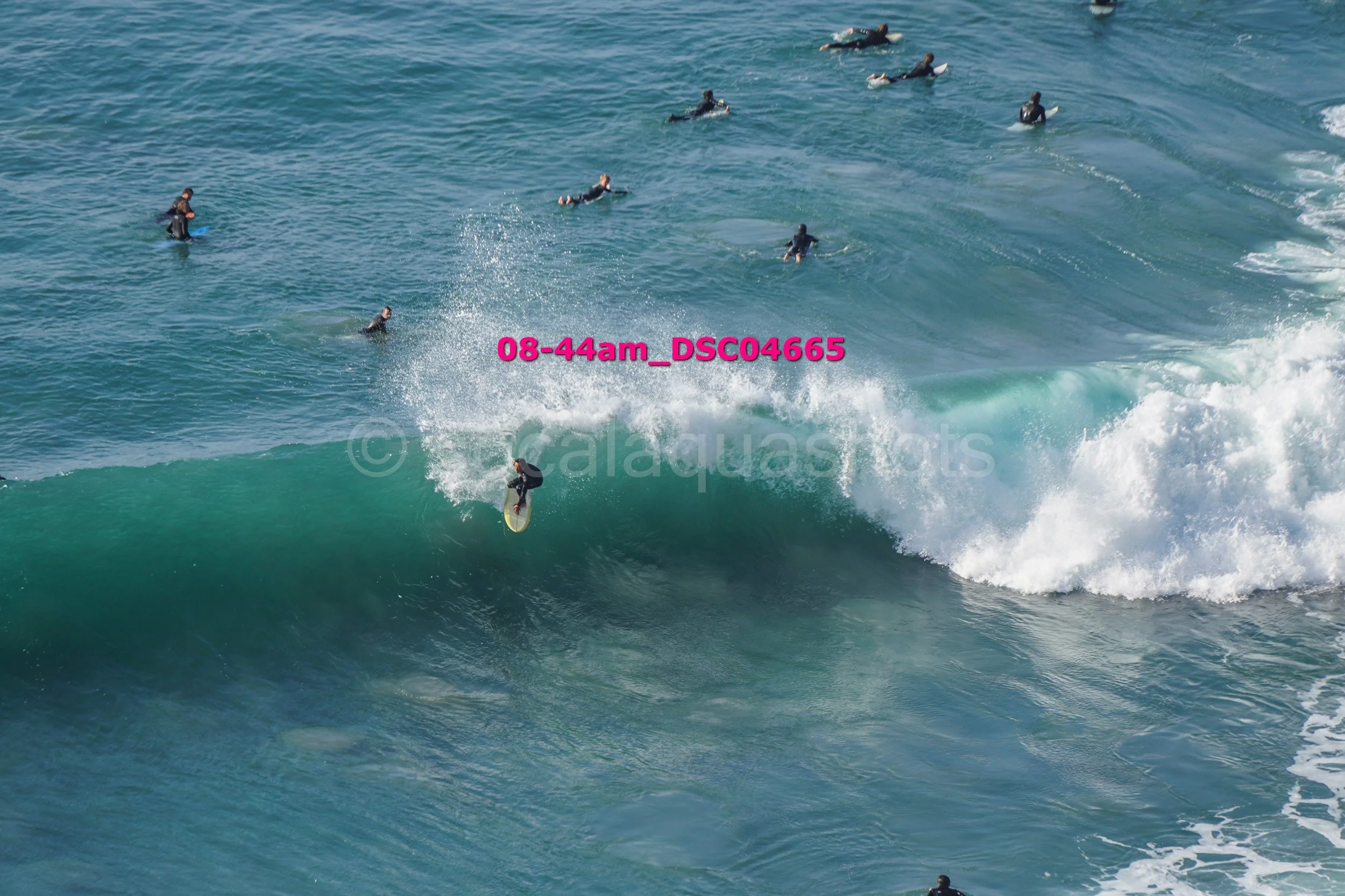 Surfer riding a large wave with multiple surfers in the water in the background.