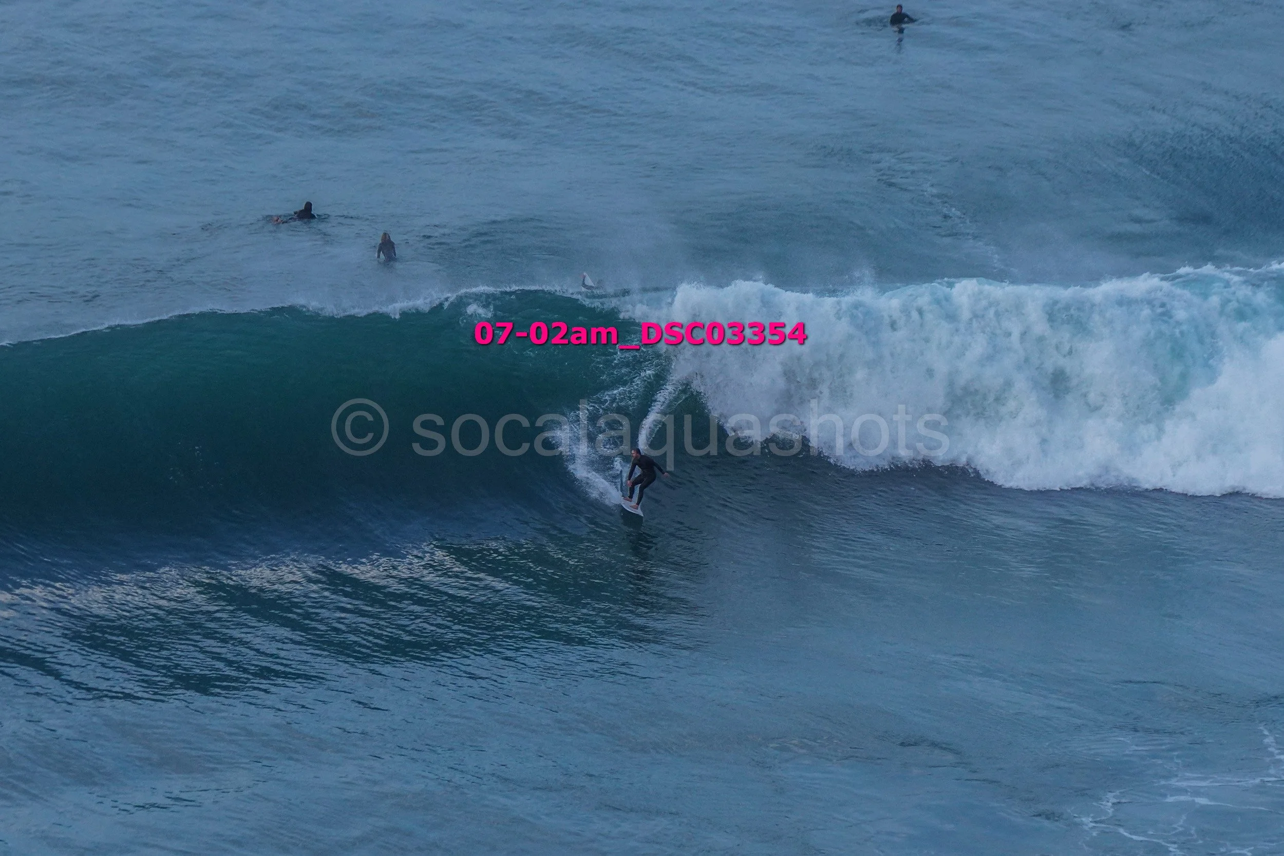 Surfer riding a wave at the beach with other surfers in the water in the background.