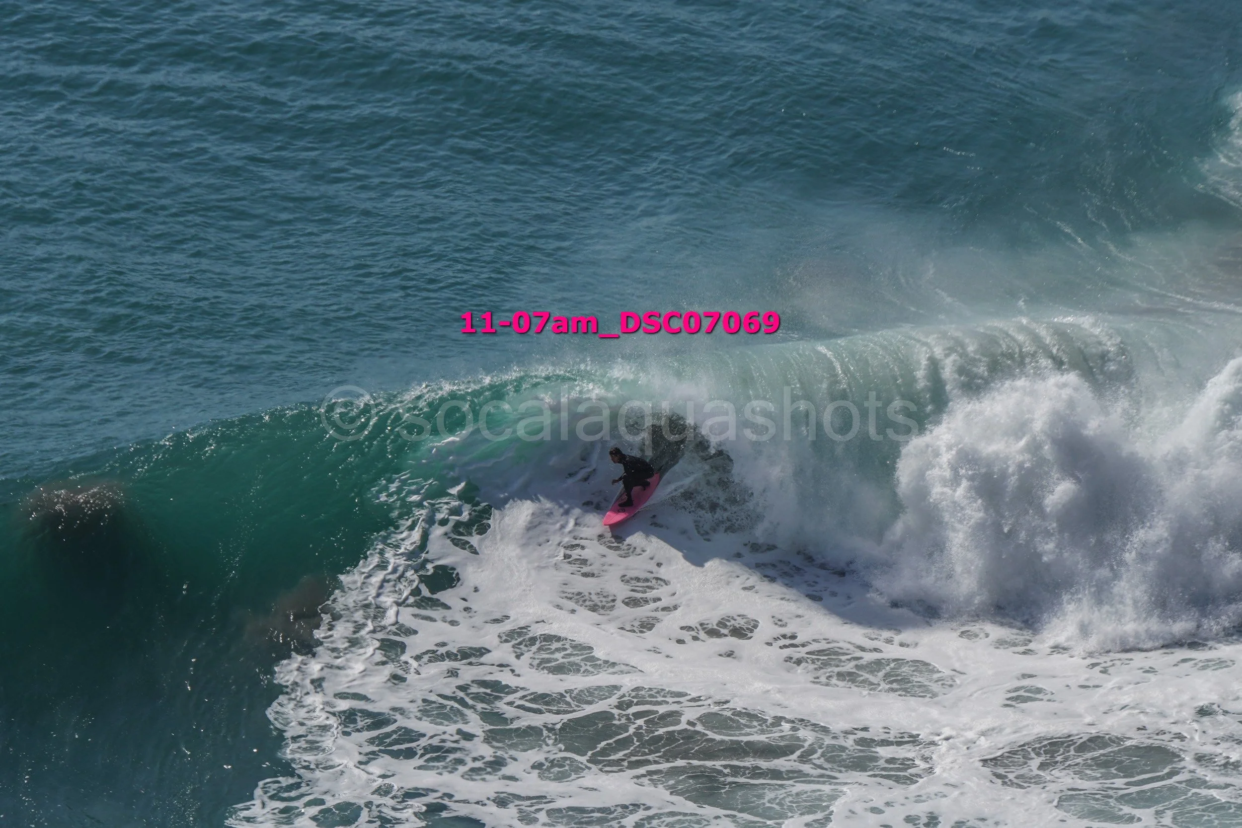 A person surfing on a pink surfboard on a large wave in the ocean.