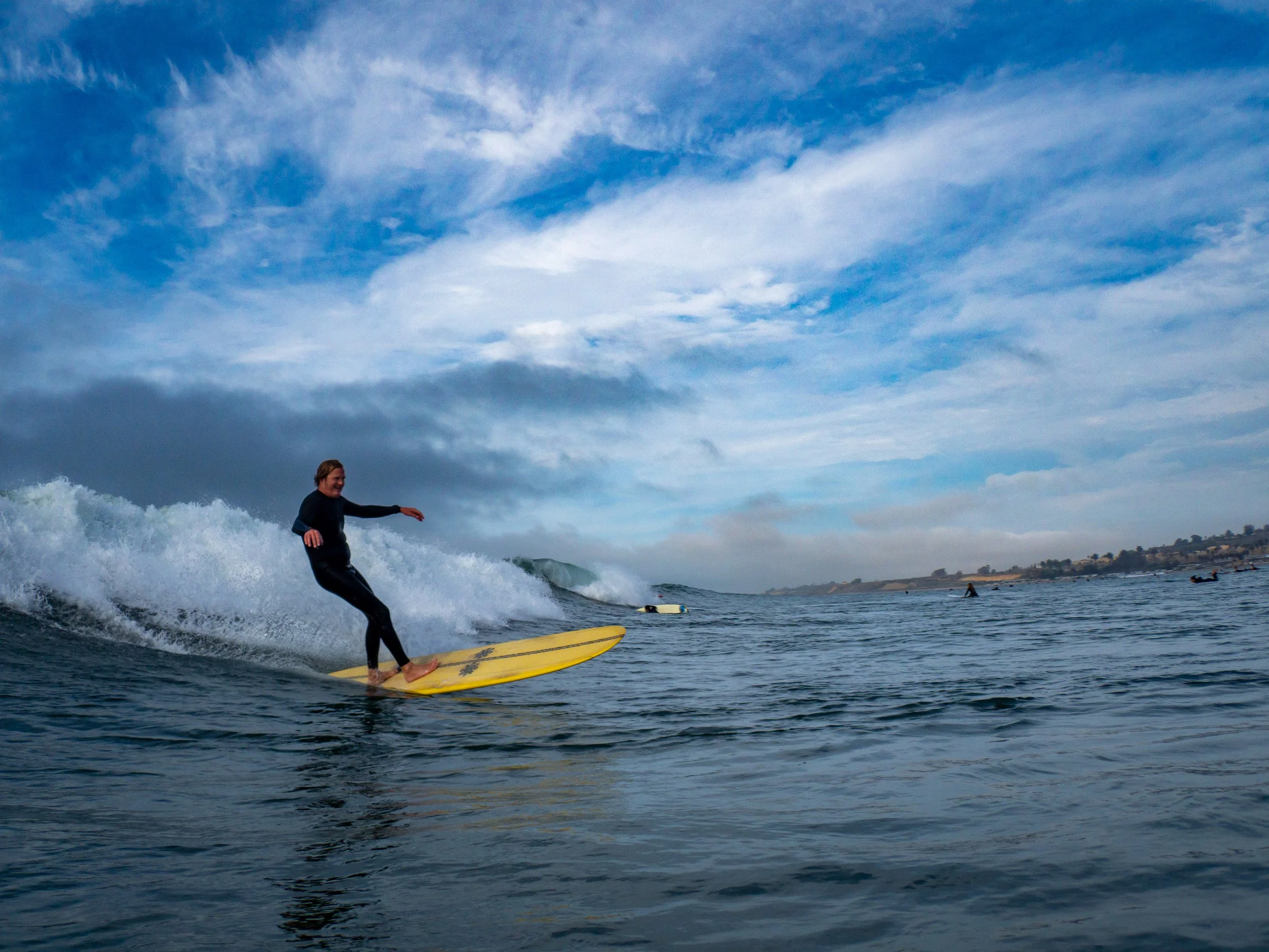 Person surfing on a yellow surfboard in the ocean with a cloudy sky overhead.