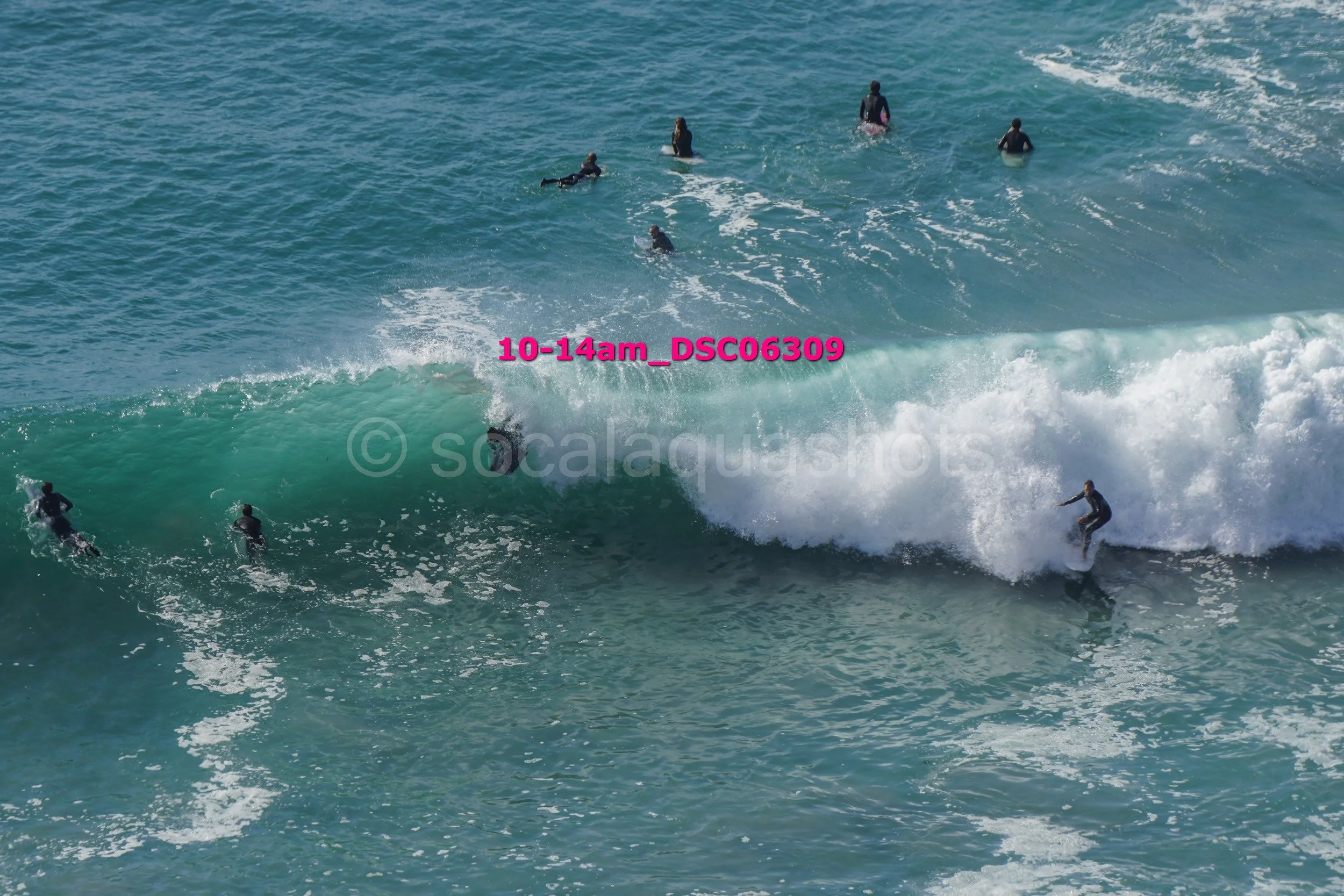 Surfer riding a wave while multiple surfers and swimmers are in the ocean around him.