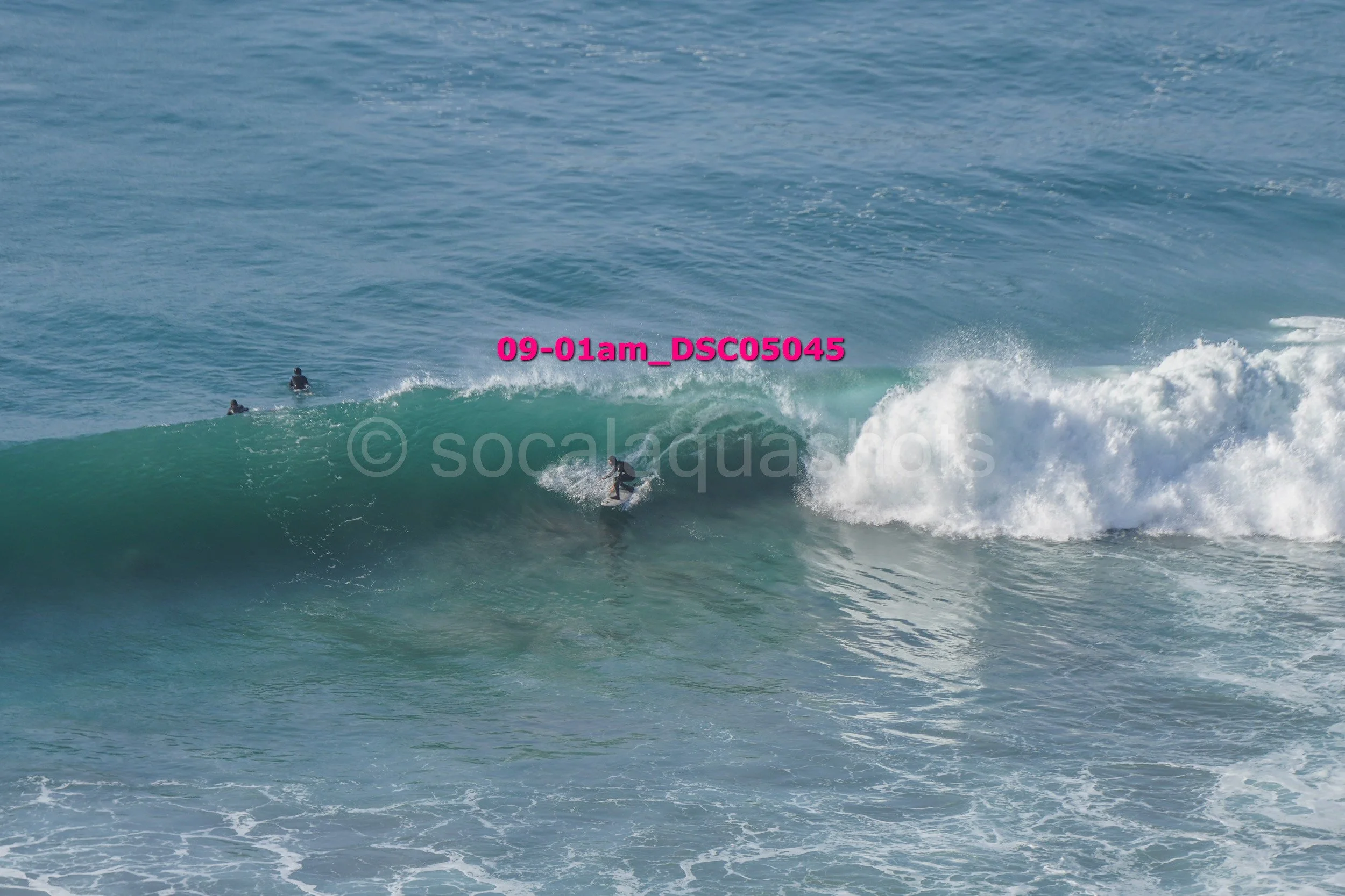 A surfer riding a wave with two other surfers in the water nearby.