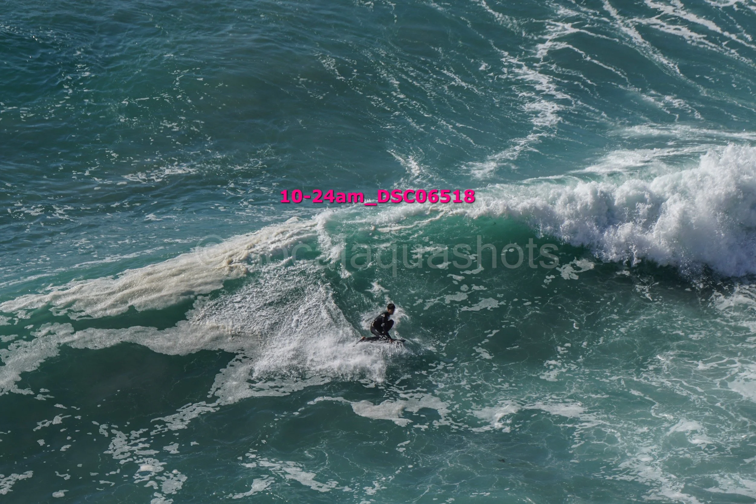 A surfer riding a wave in the ocean with white frothy water and blue-green sea.
