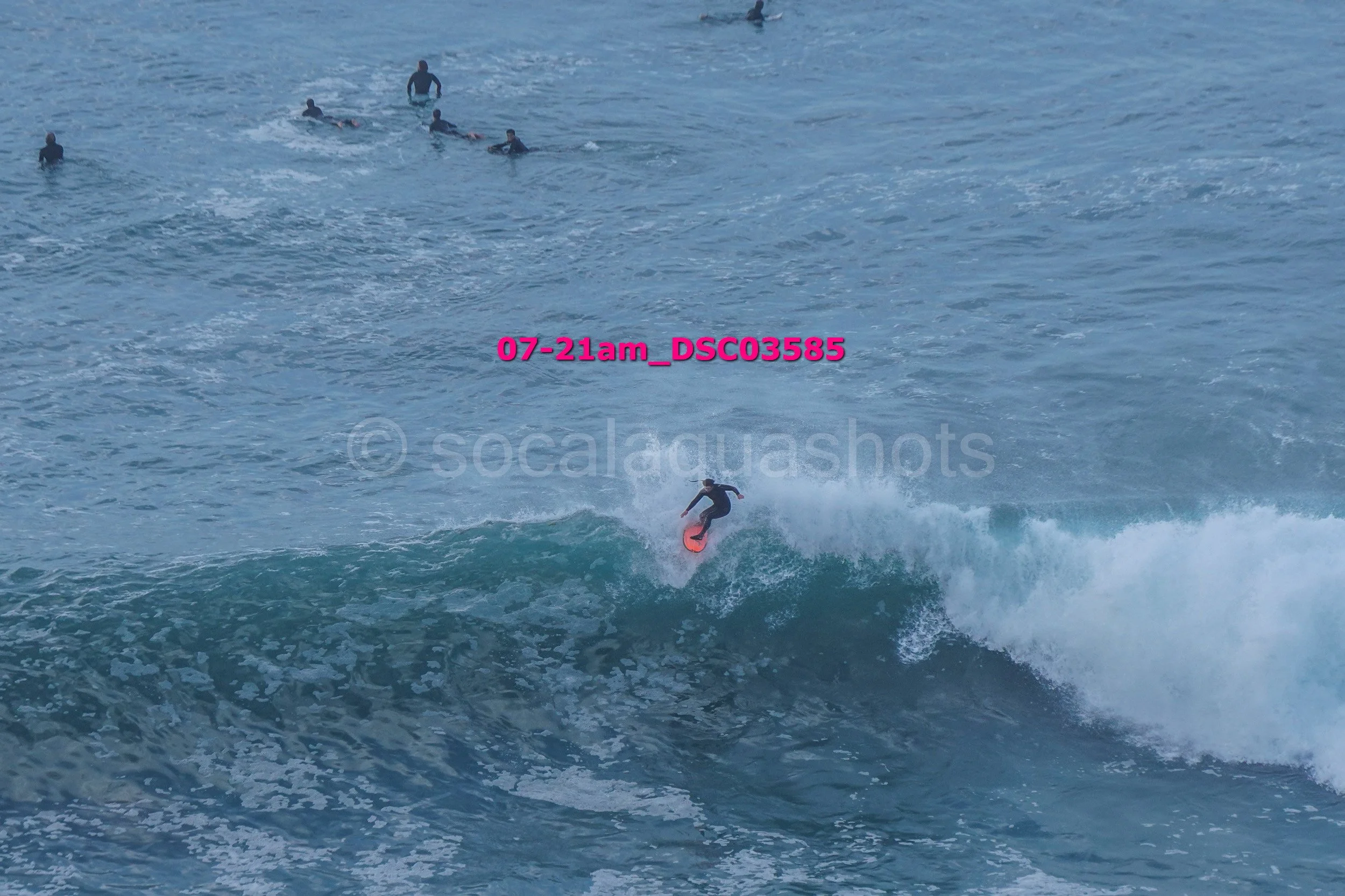 Surfer riding a wave with a group of surfers in the water in the background.
