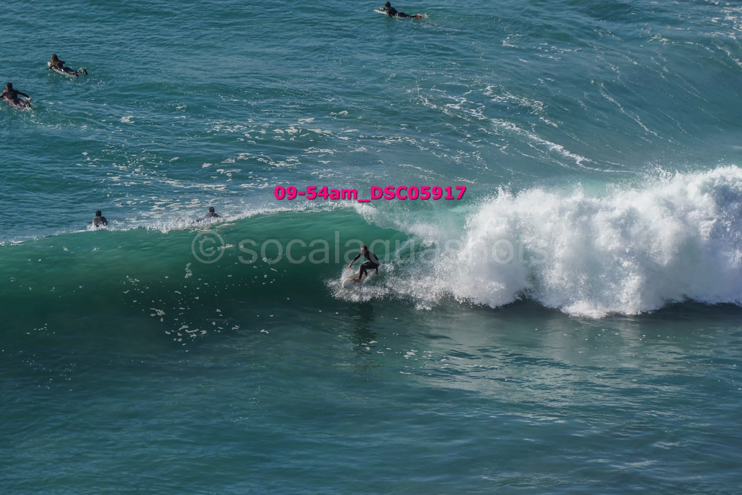 Surfer riding a wave at the beach with several people swimming in the background.