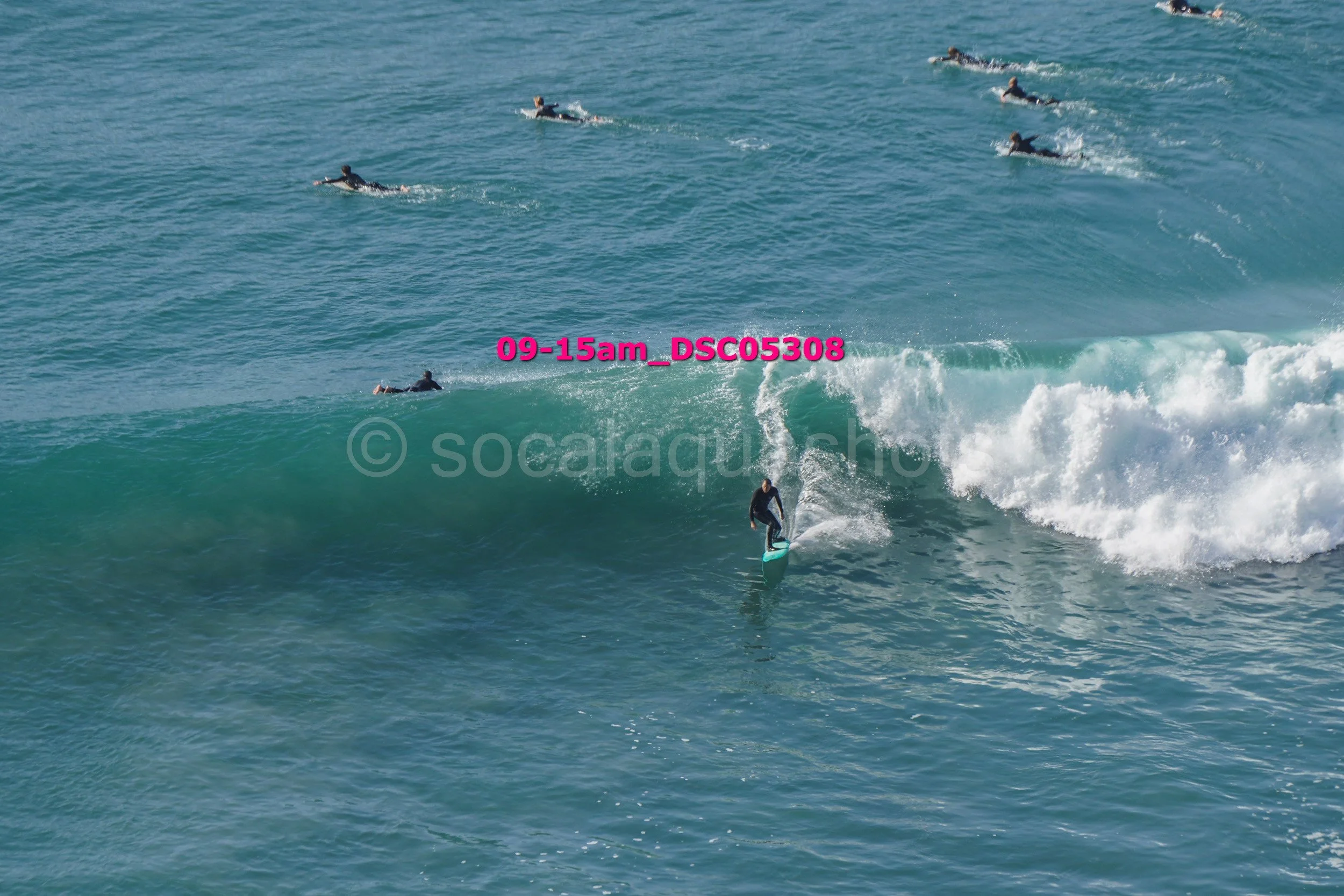 A person surfing on a turquoise wave with several other surfers in the water in the background.