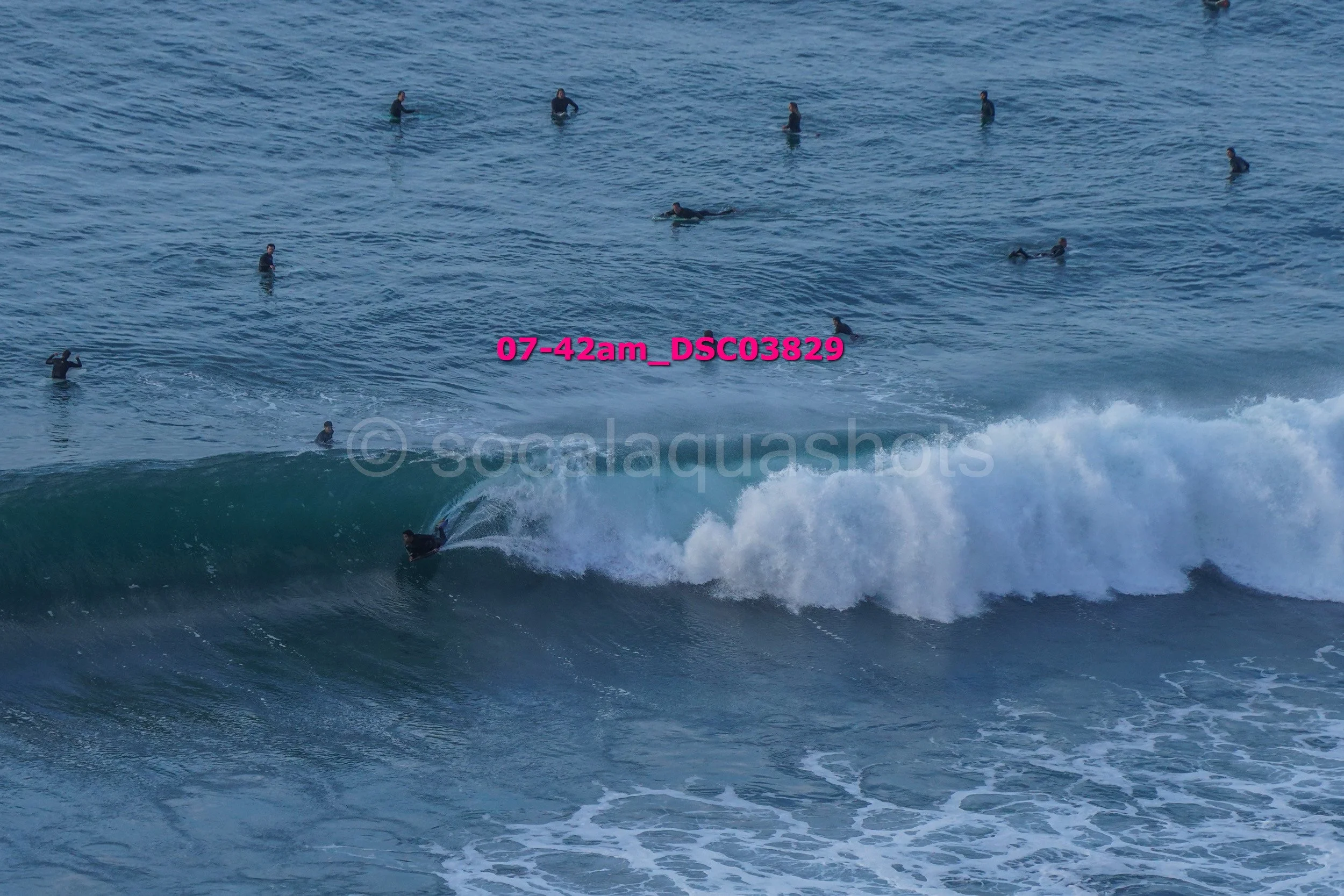 Surfer riding a wave with several surfers in the water nearby, on a cloudy day.