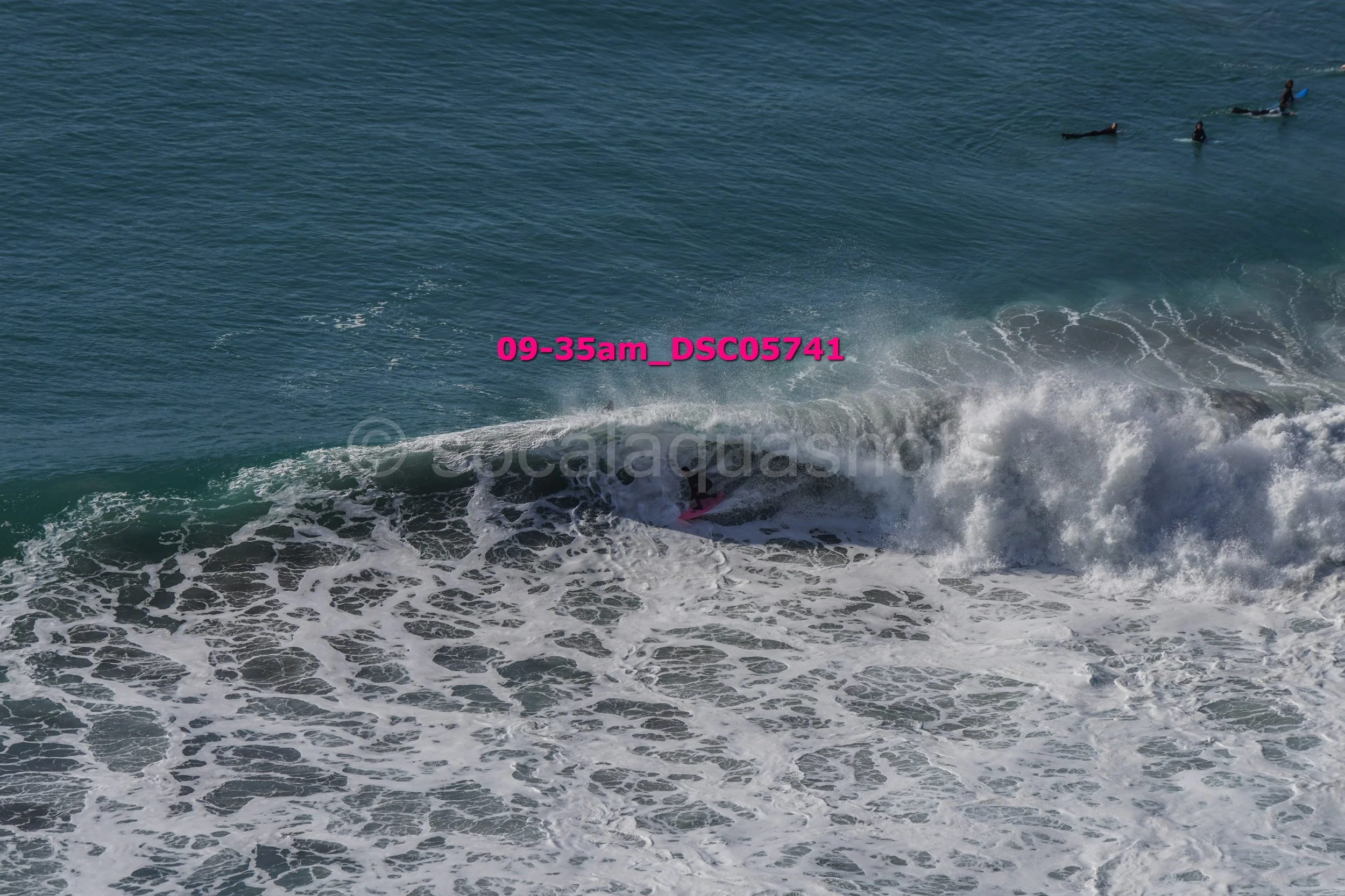 Surfer riding a wave in the ocean with four surfers floating on their boards in the background.