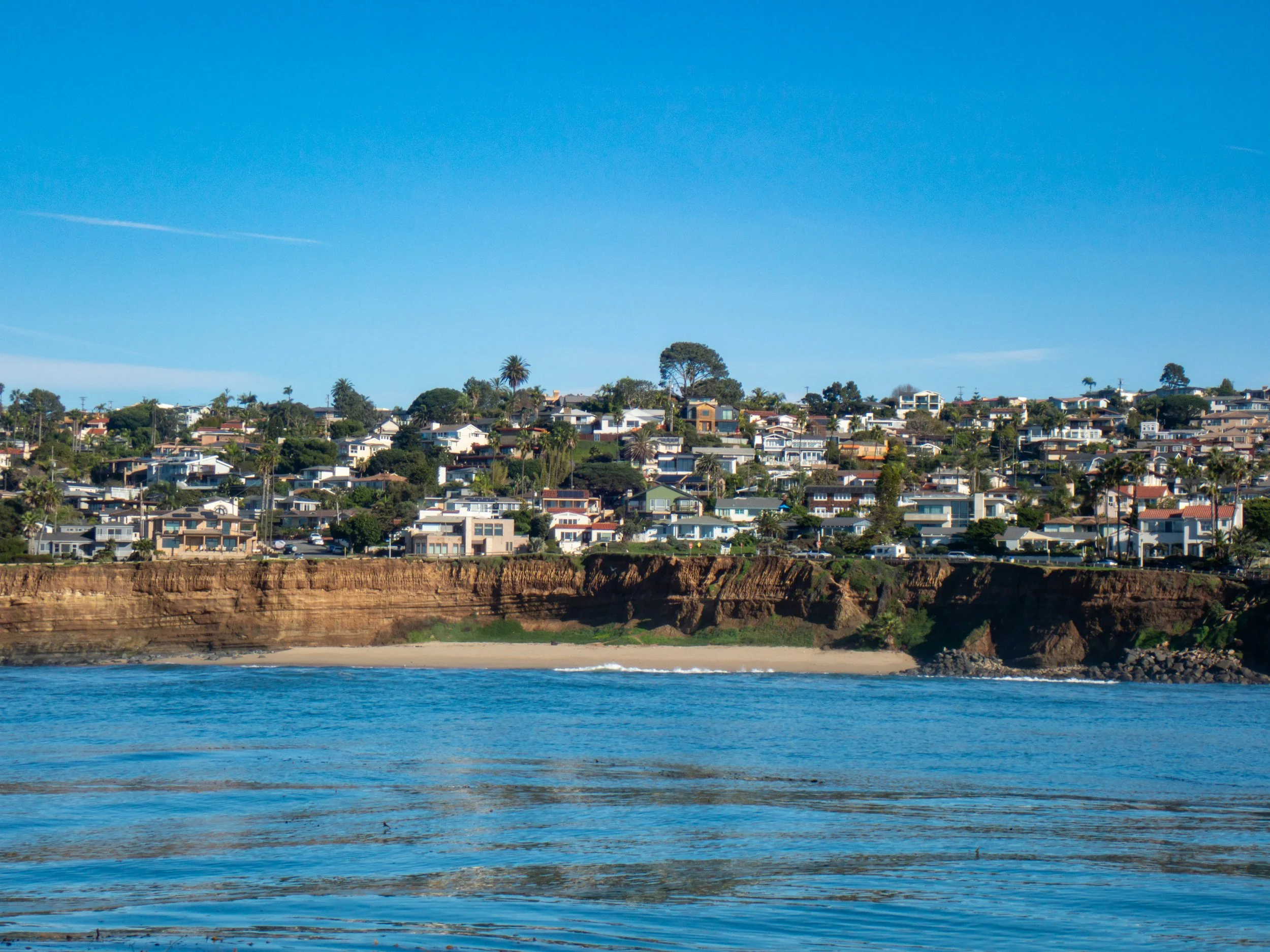 Houses and buildings on a hillside overlooking the ocean with clear blue sky.
