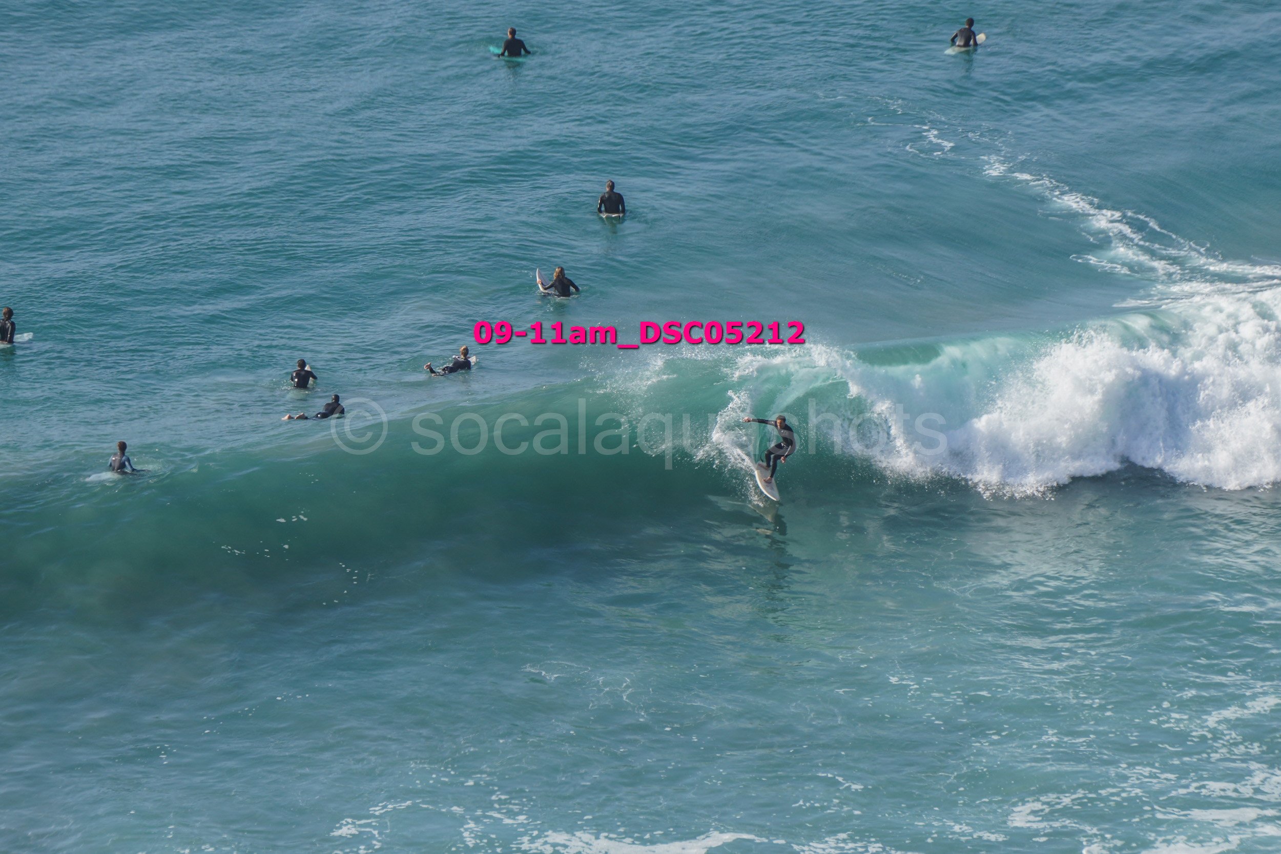 A surfer riding a wave at the beach, with multiple surfers in the water around him.
