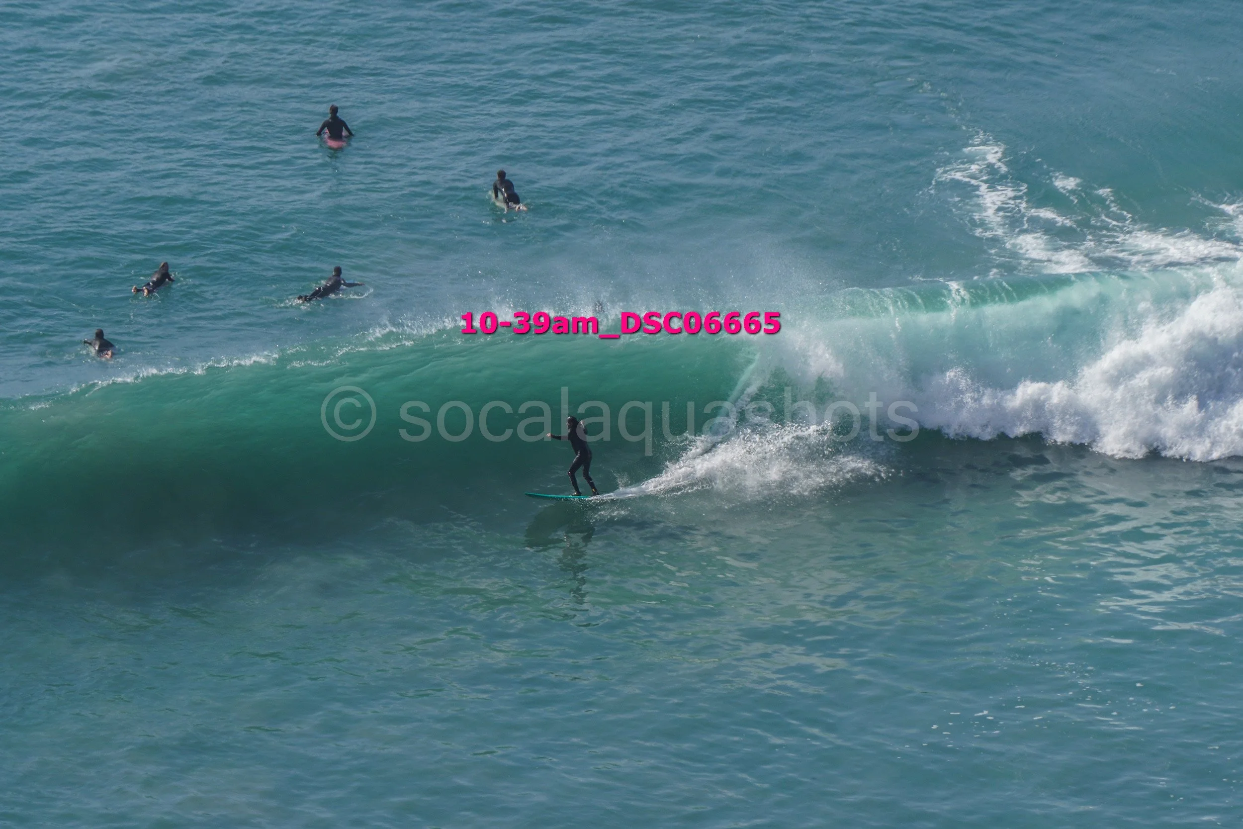 A person surfing a wave while others swim nearby in the ocean.