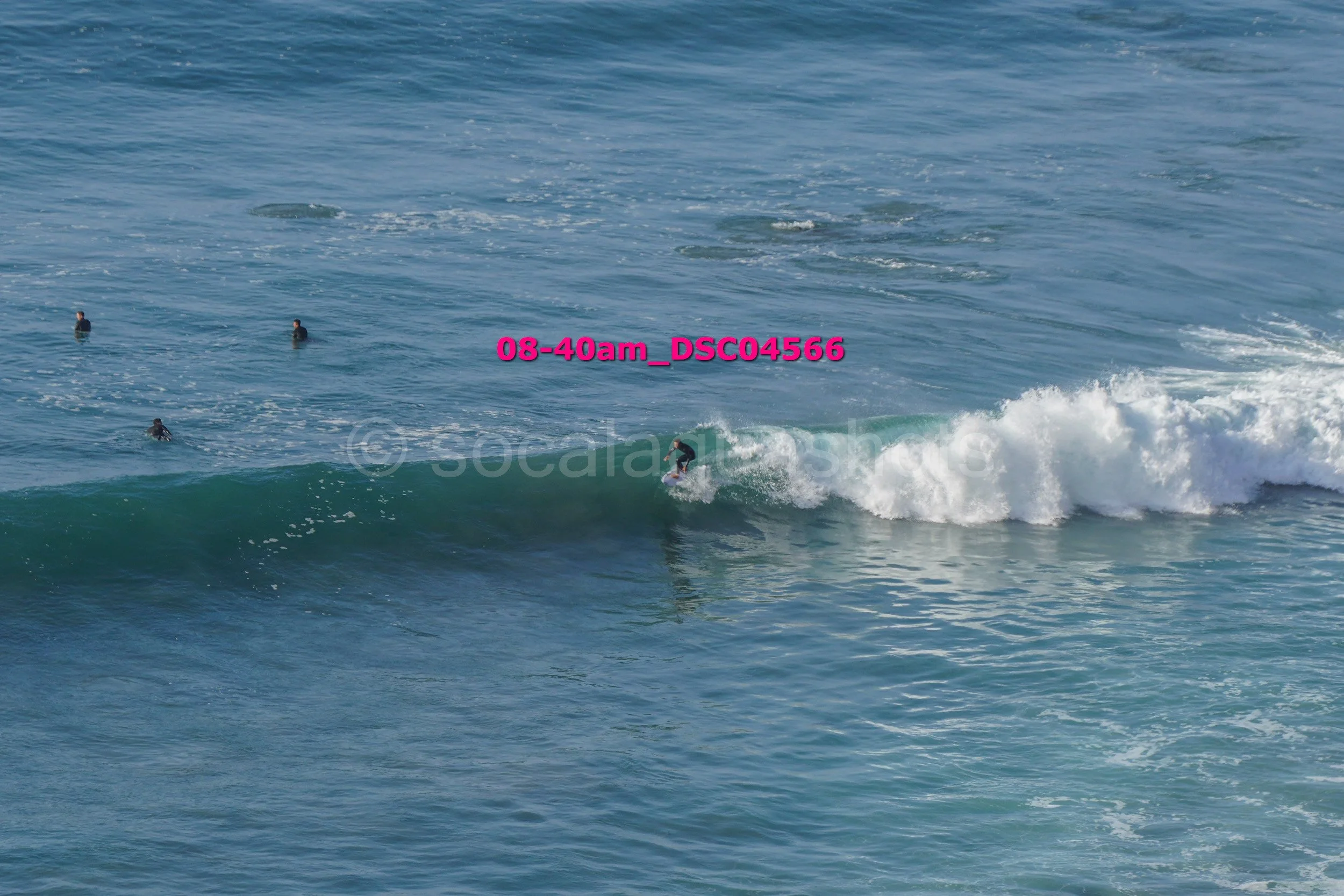 A person surfing on a wave in the ocean with several people in the water nearby.