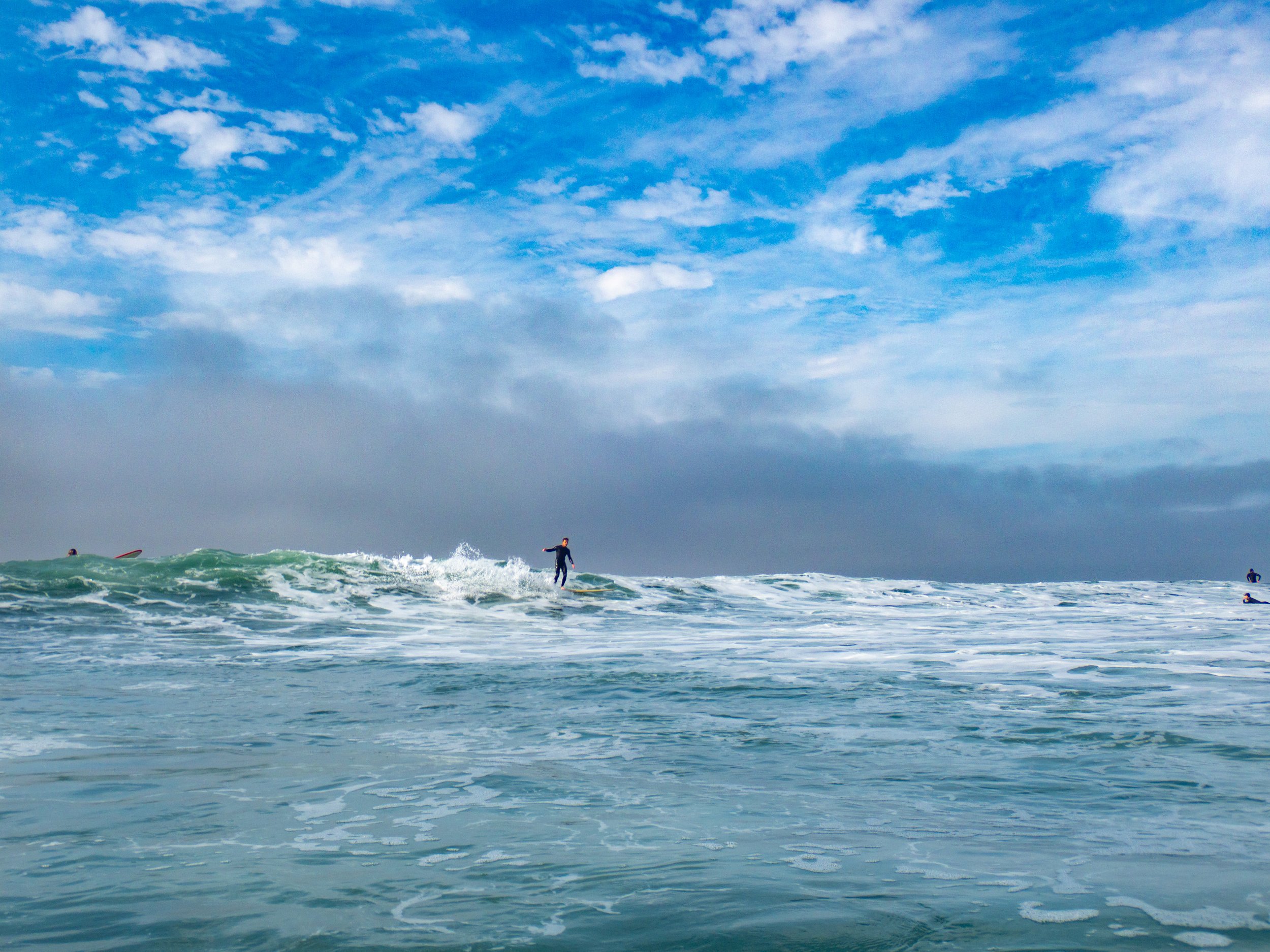 A person surfing on a wave in the ocean with a blue sky and scattered clouds in the background.