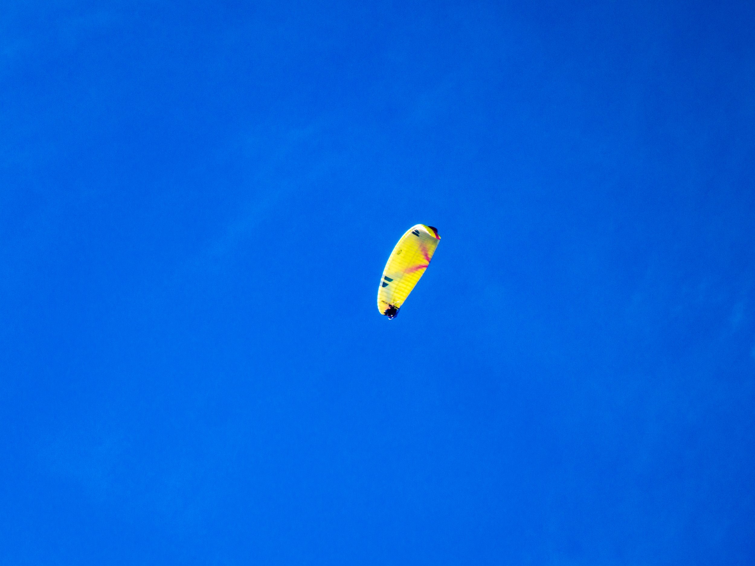 A person paragliding with a yellow parachute against a clear blue sky.