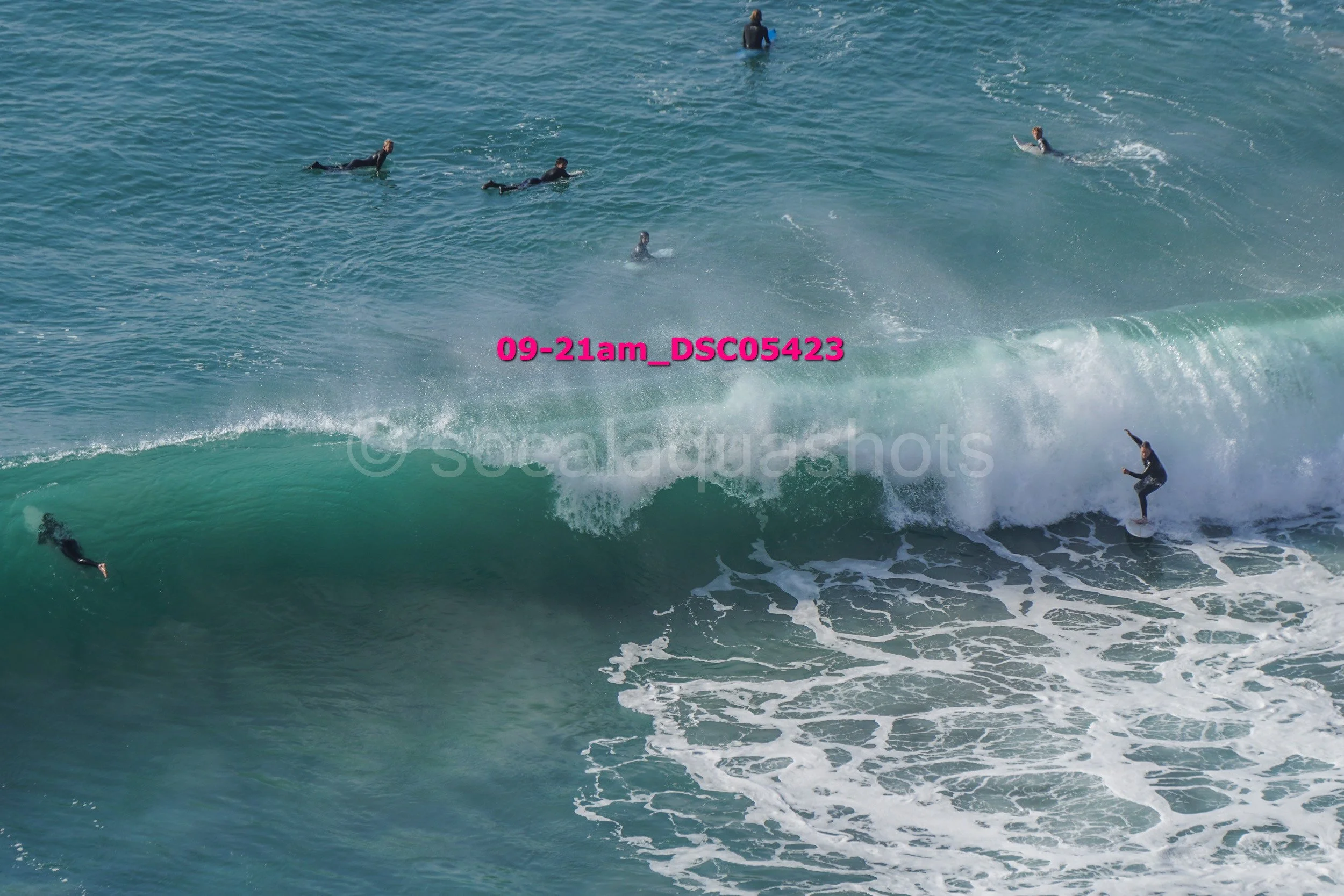 Surfers riding and paddling on ocean waves during daytime.