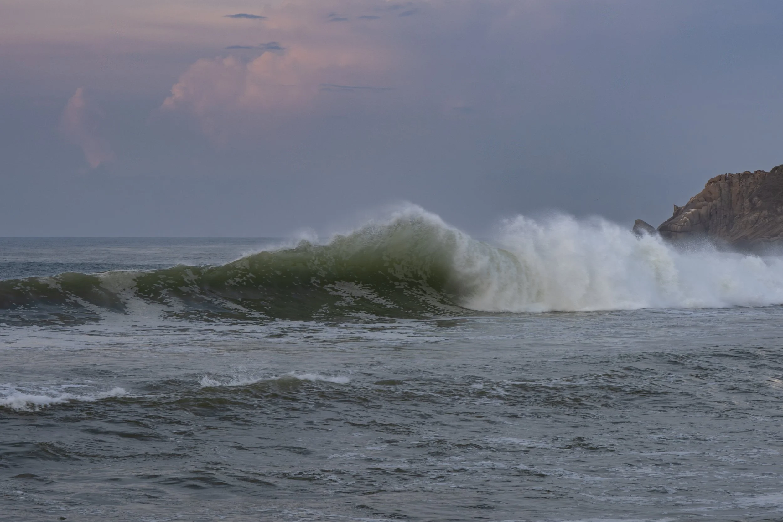 Ocean waves crashing near a rocky cliff during overcast weather.