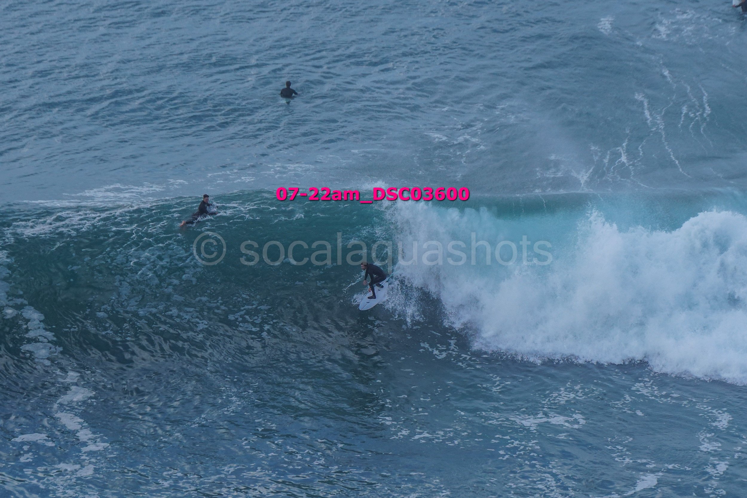 A person surfing on a wave with three other surfers visible in the background in the ocean.