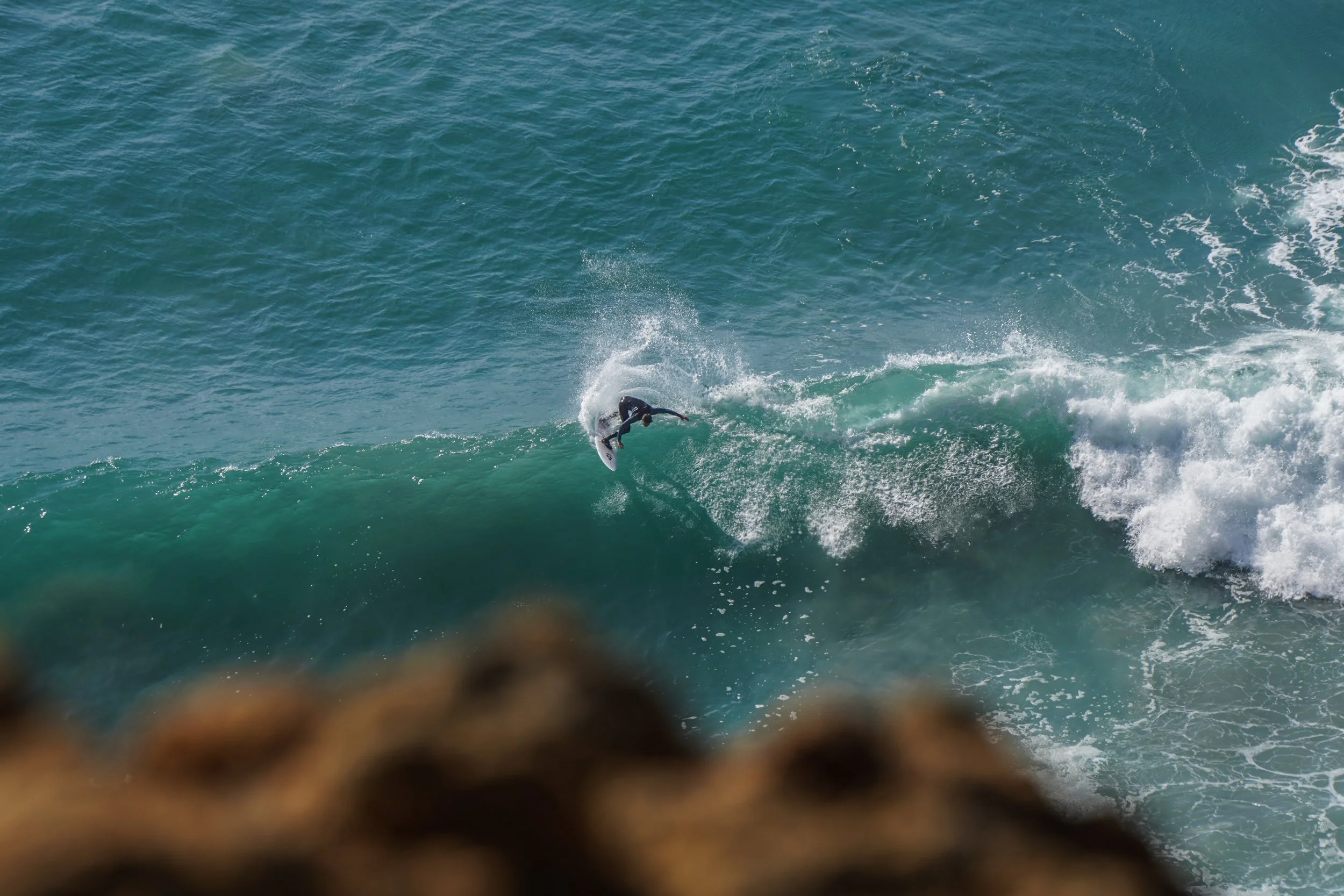A person in a wetsuit surfing on a large ocean wave, with the sea and sky in the background.