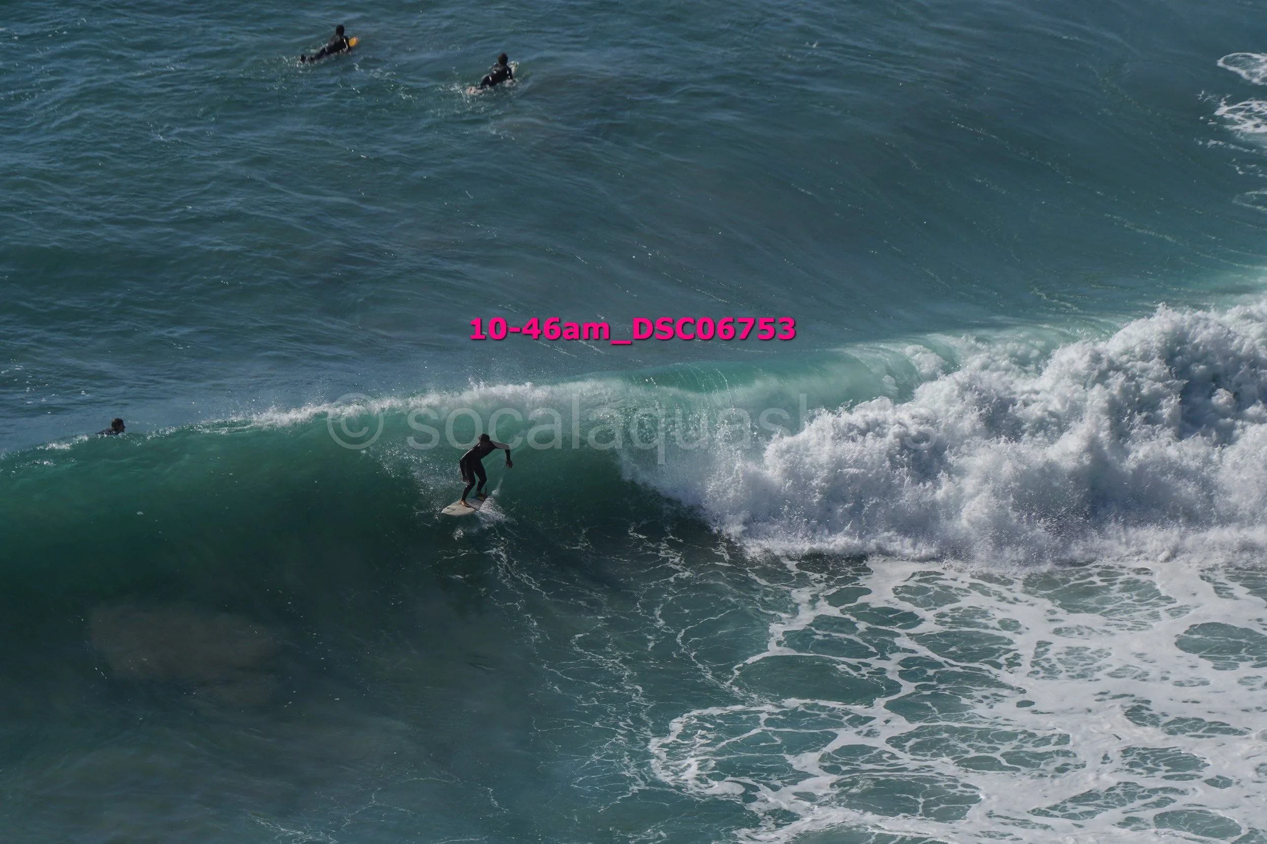 A person surfing on a wave with three other people in the water nearby.