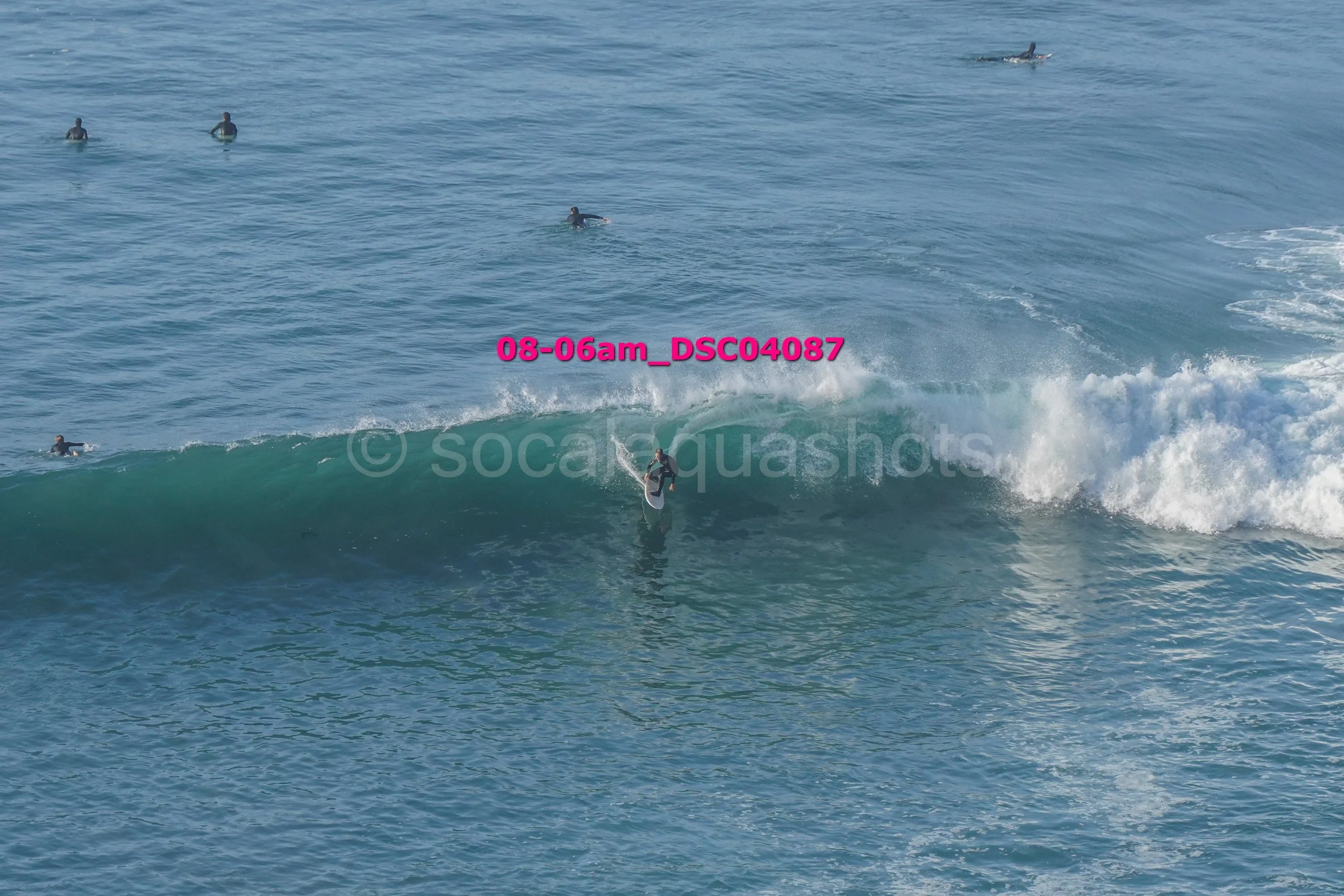 A person surfing on a wave with several others in the water