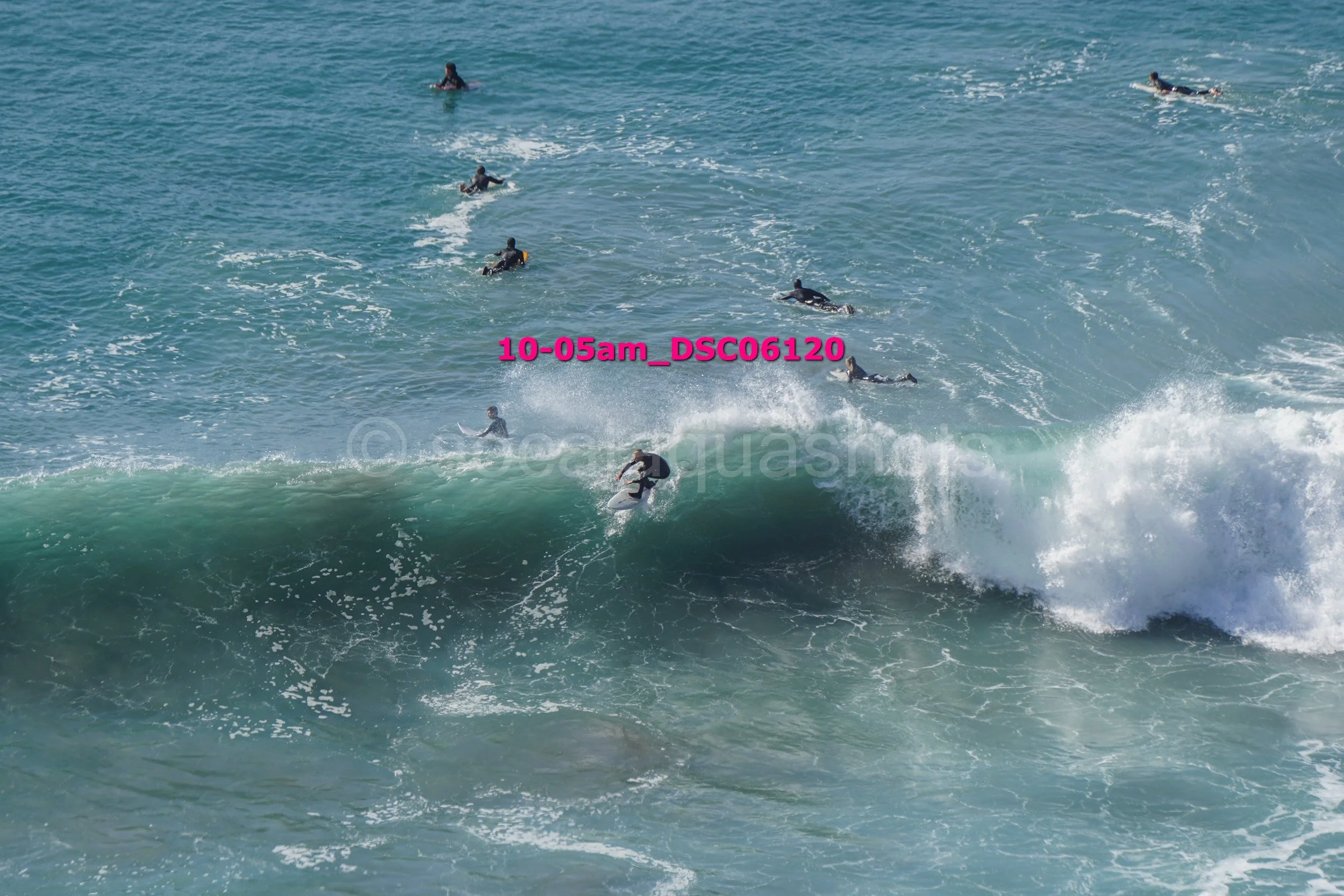 Surfers riding and waiting on ocean waves with some surfers in the background and spray from the waves.