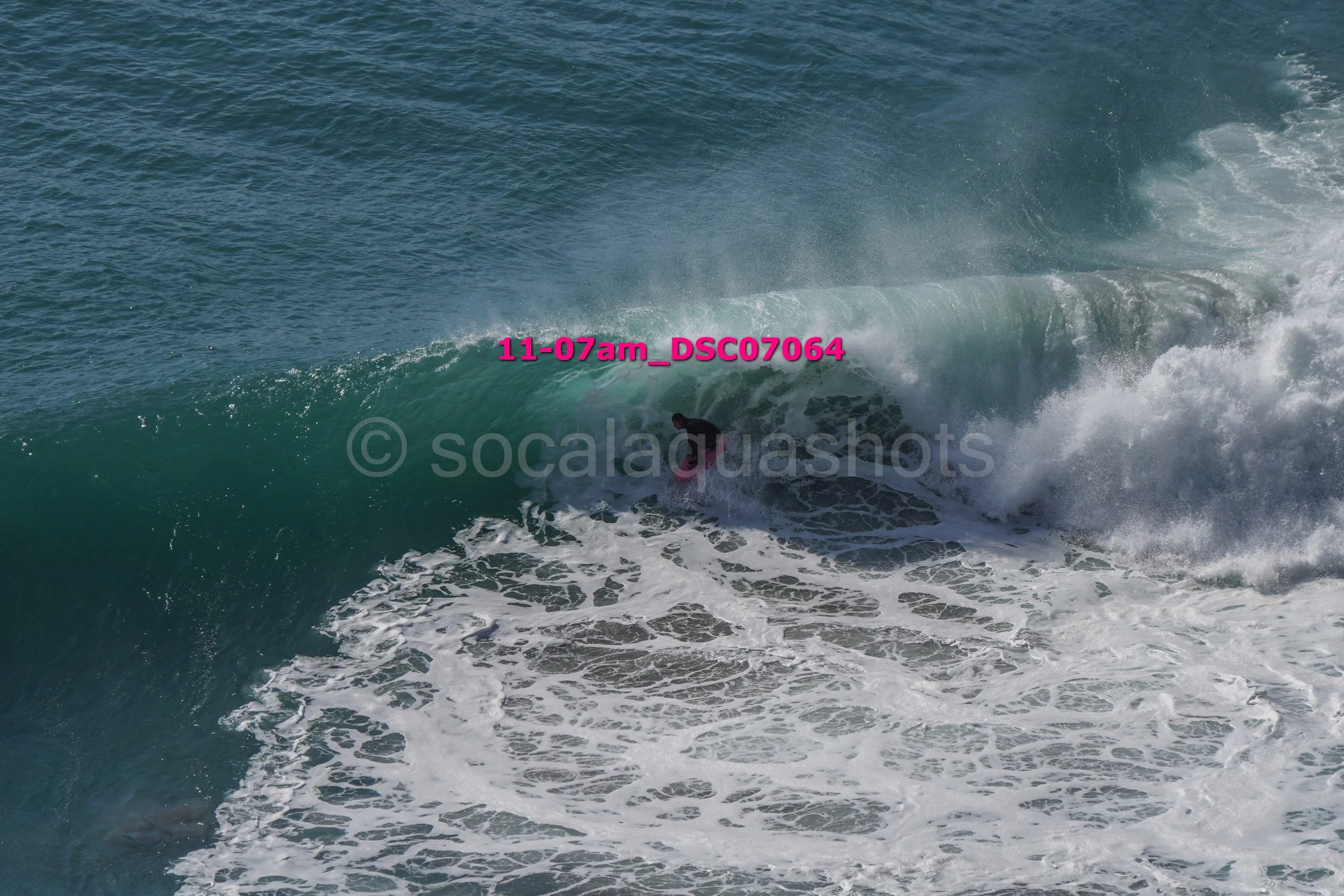 A surfer riding inside a large ocean wave with white foam and water spray.