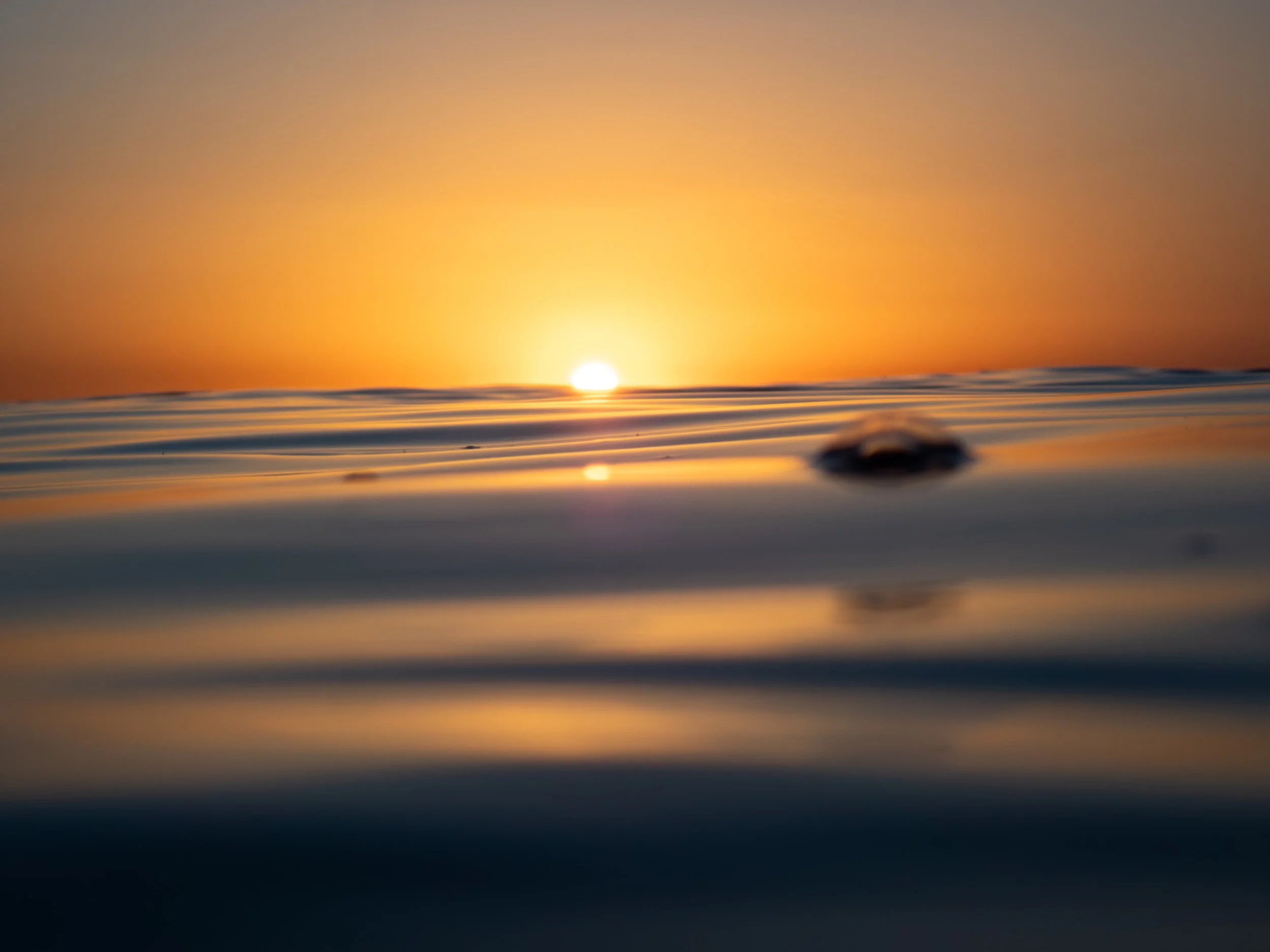 A sunset over the ocean, with the sun near the horizon and gentle waves in the foreground.