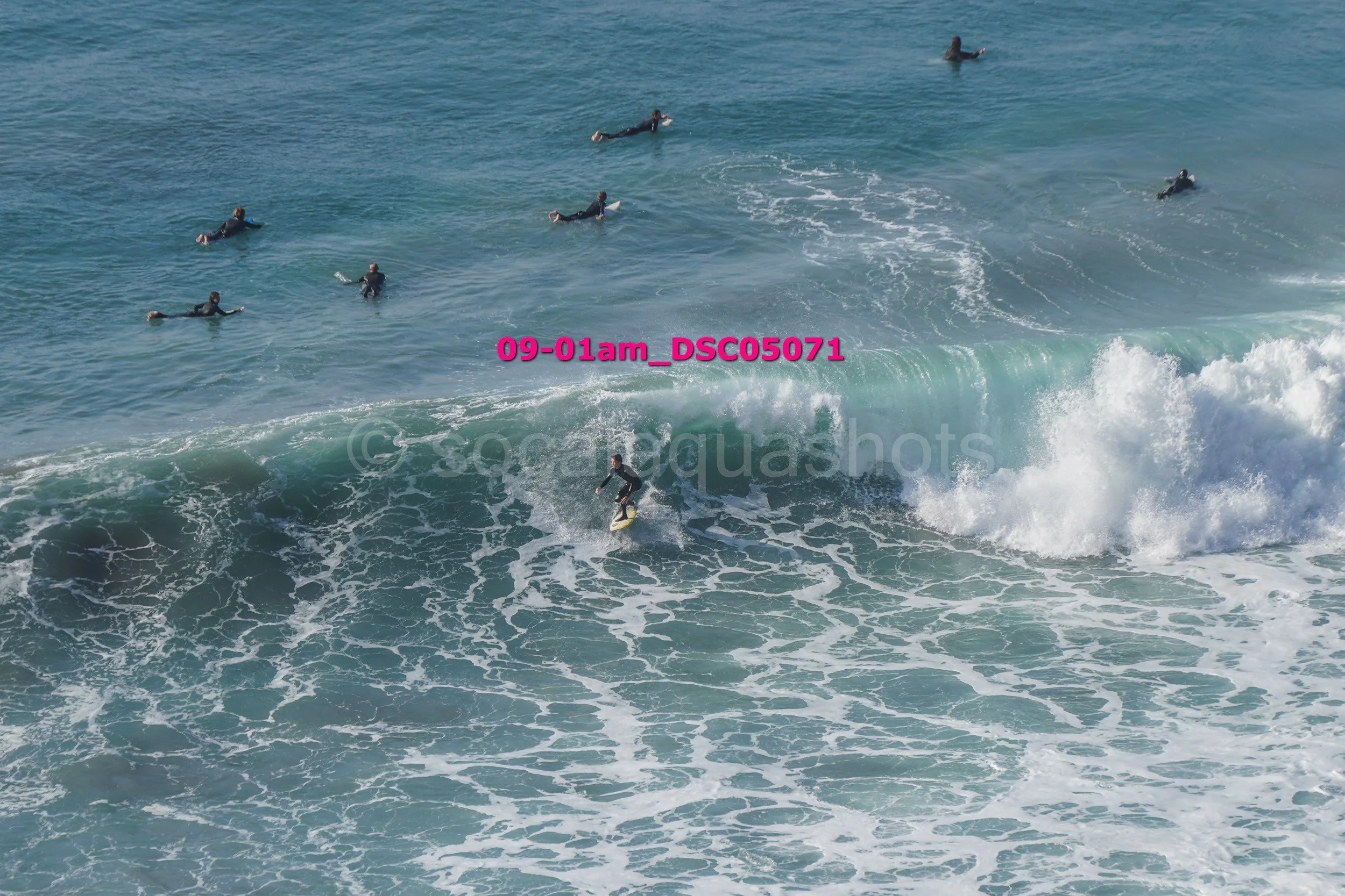 A person surfing on a wave at the beach with several swimmers in the water nearby.