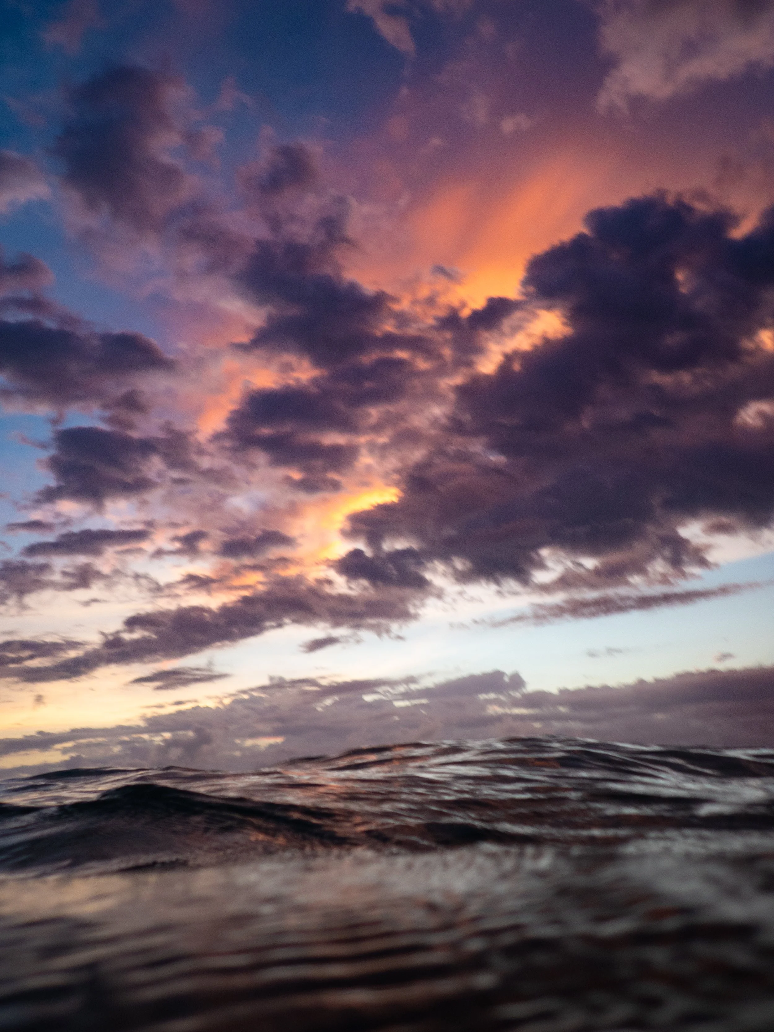 Sunset sky with dark clouds and a hint of orange and pink, viewed from the water's surface.