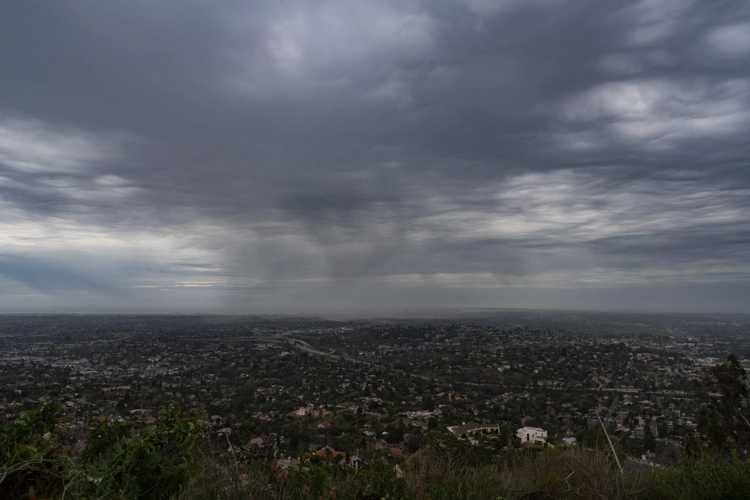 A wide view of a cityscape under dark stormy clouds with rain in the distance.