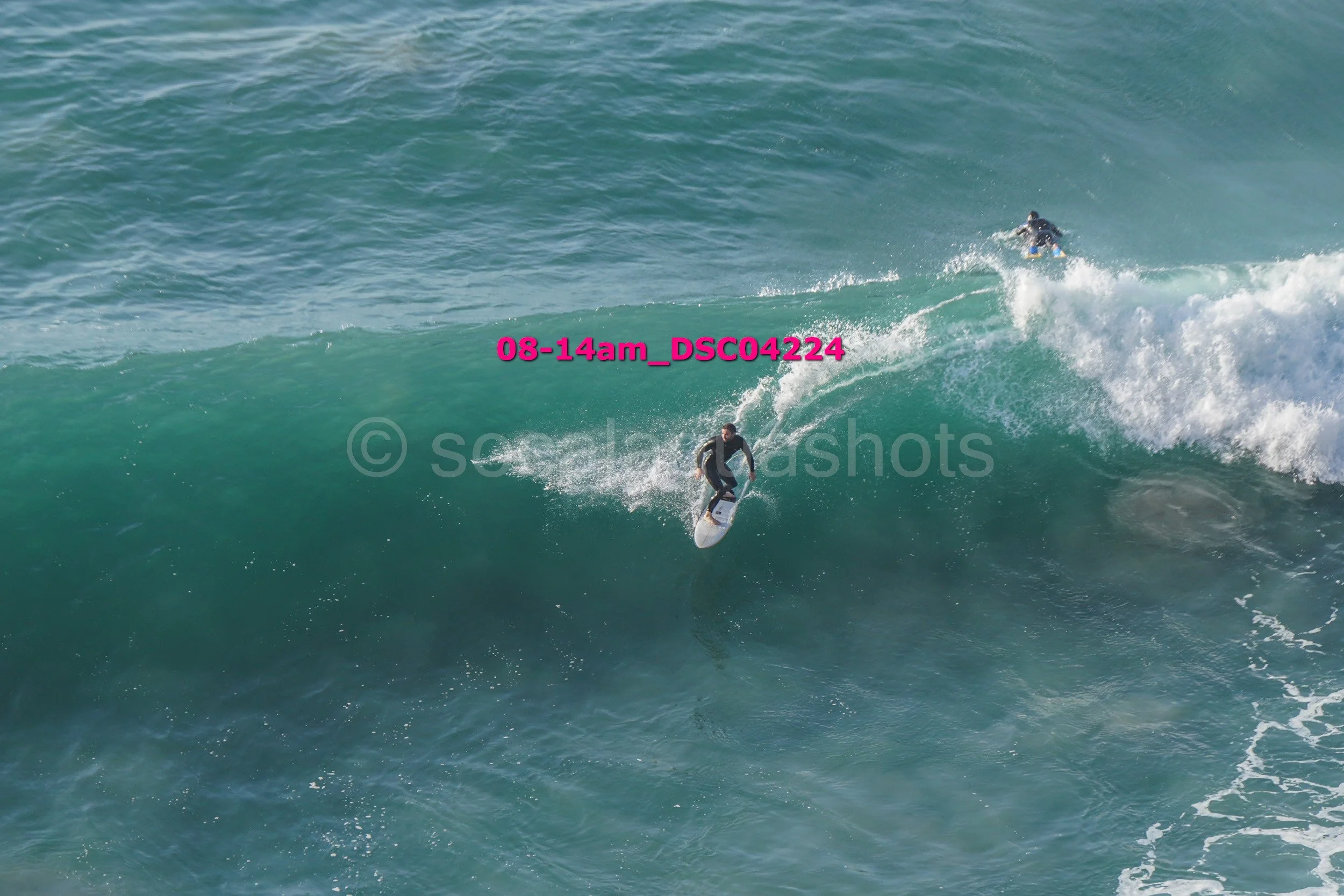 A person surfing on a large wave in the ocean with another surfer in the distance.