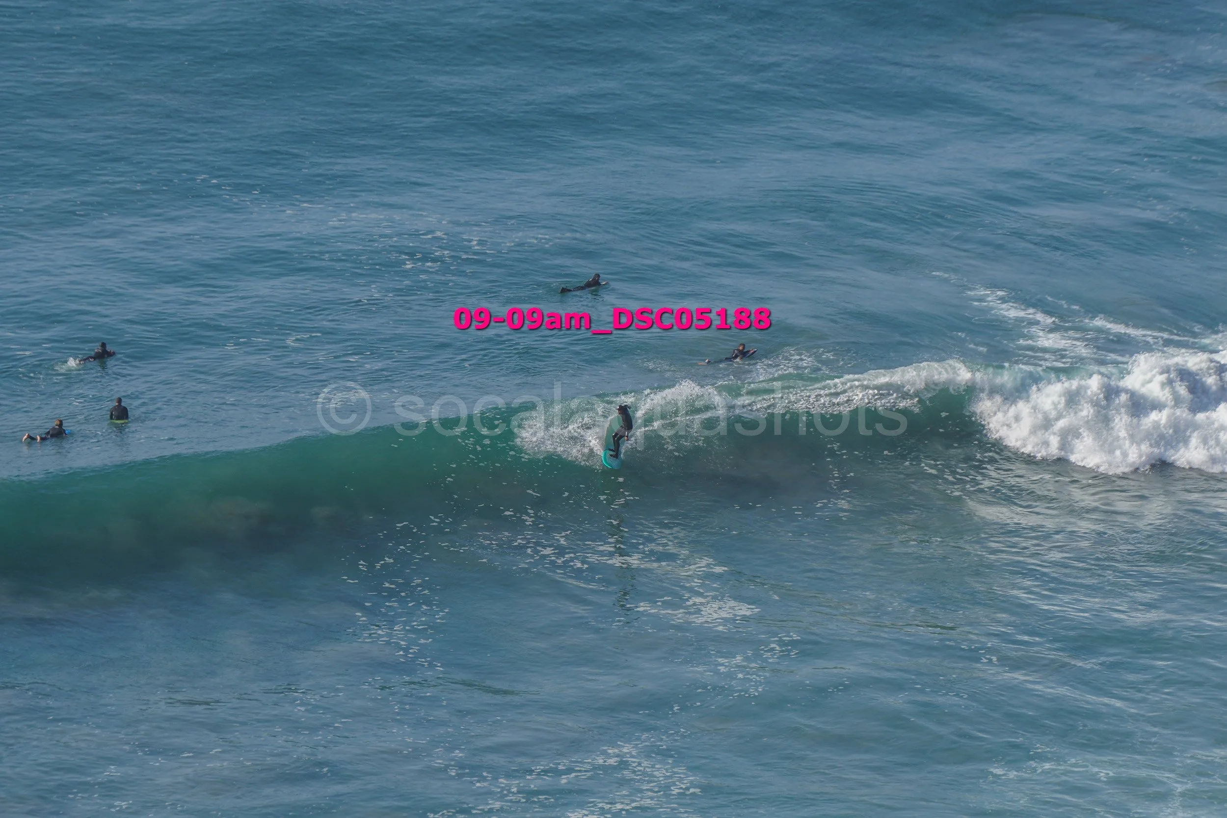 A person surfing on a wave while several other surfers are floating in the water nearby.