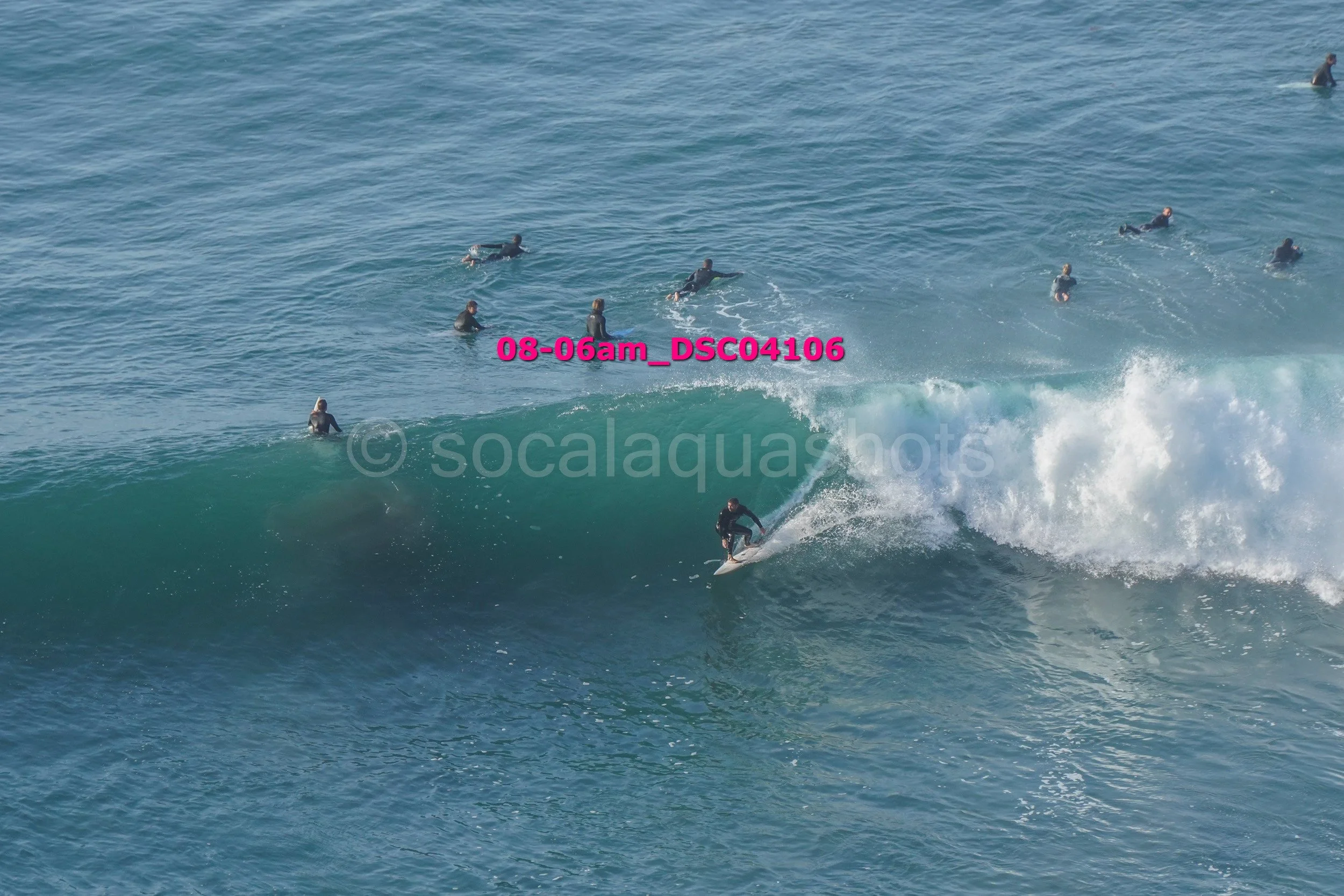 A surfer riding a wave while surrounded by several surfers in the water, with some waiting to catch a wave.