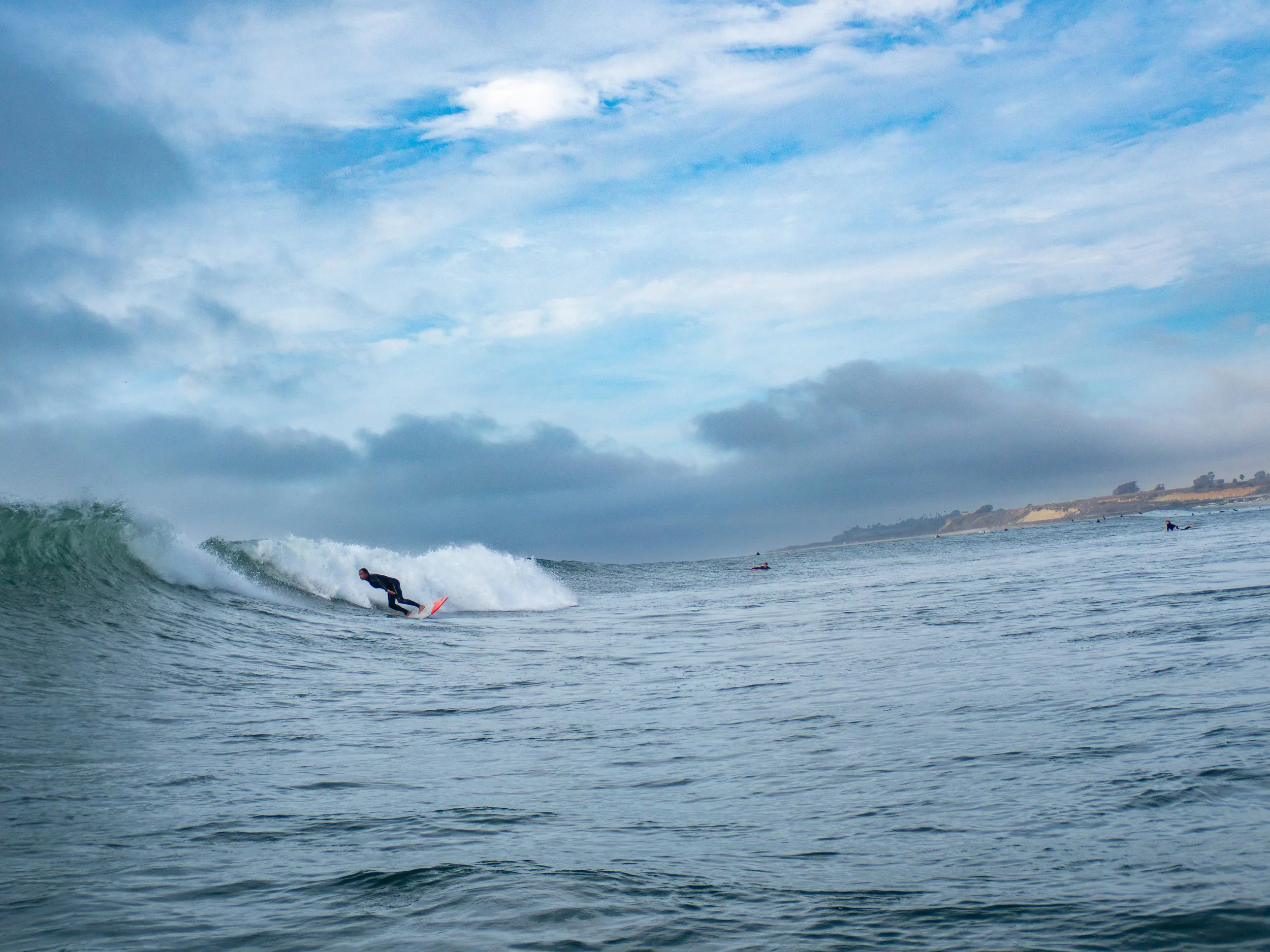 A surfer riding a wave in the ocean with a cloudy sky and land in the background.