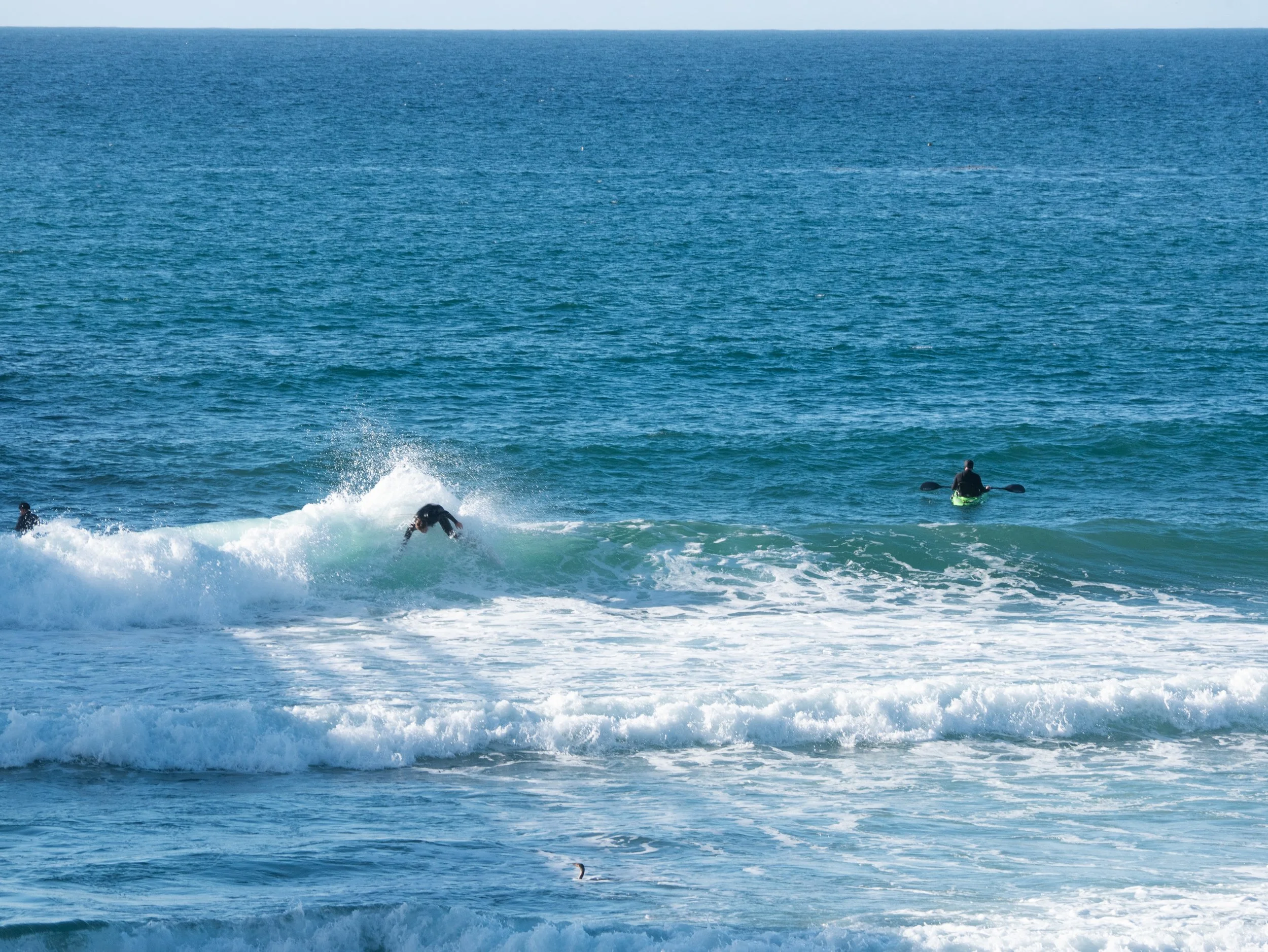 Group of people surfing and kayaking in the ocean on a sunny day.
