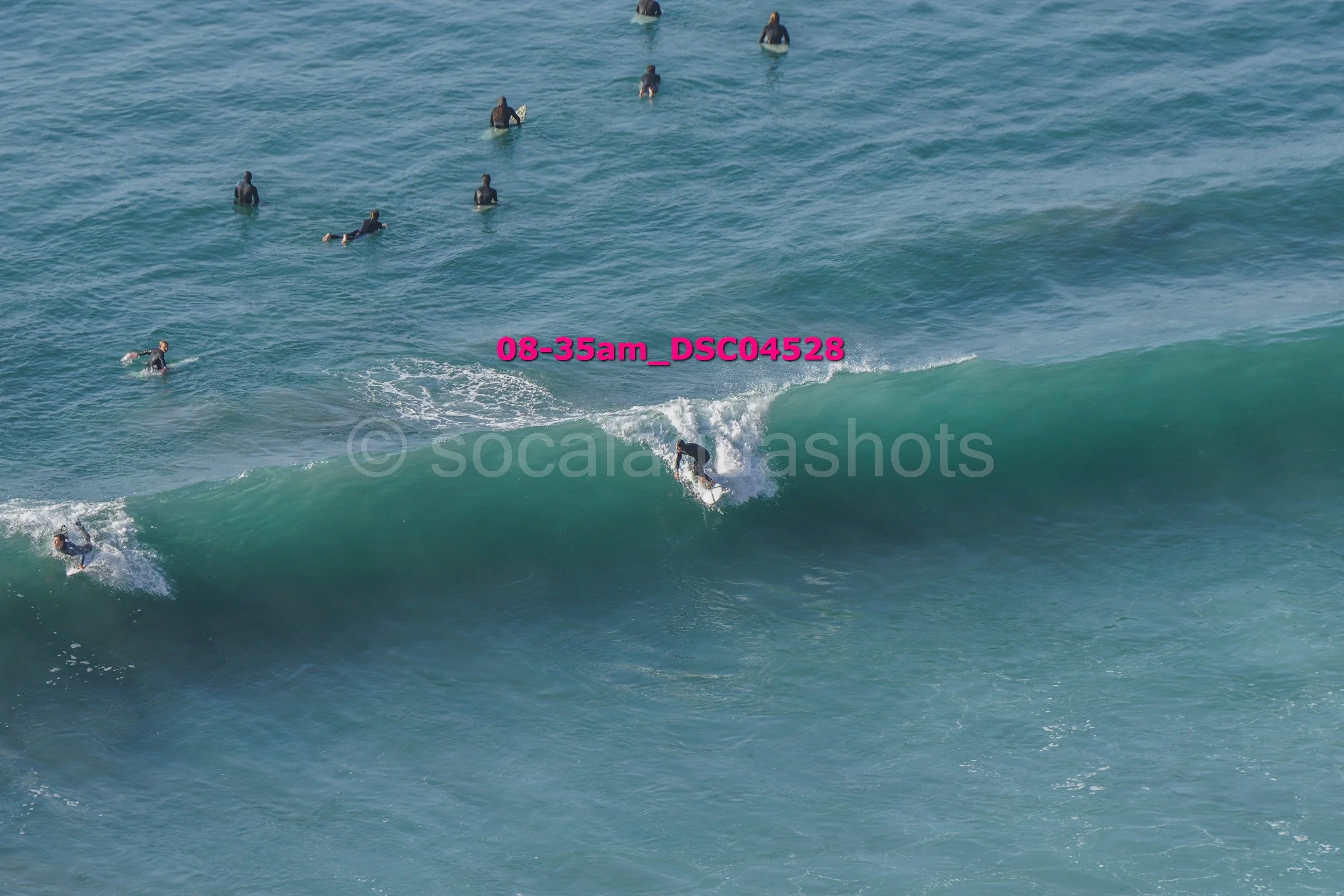 Surfer riding a wave with several people swimming and surfing in the background in the ocean.