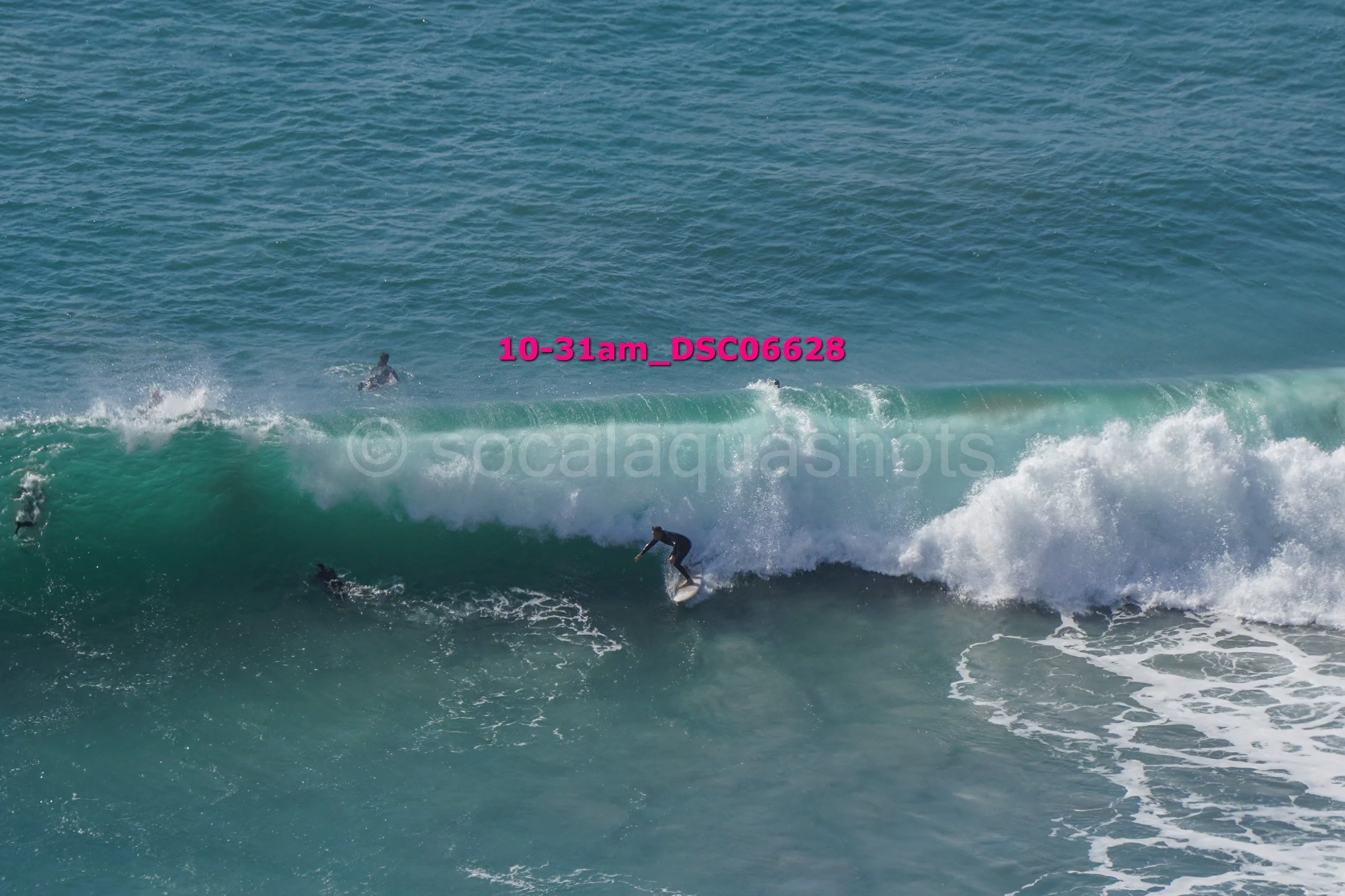 Surfer riding a large ocean wave with other surfers in the background.