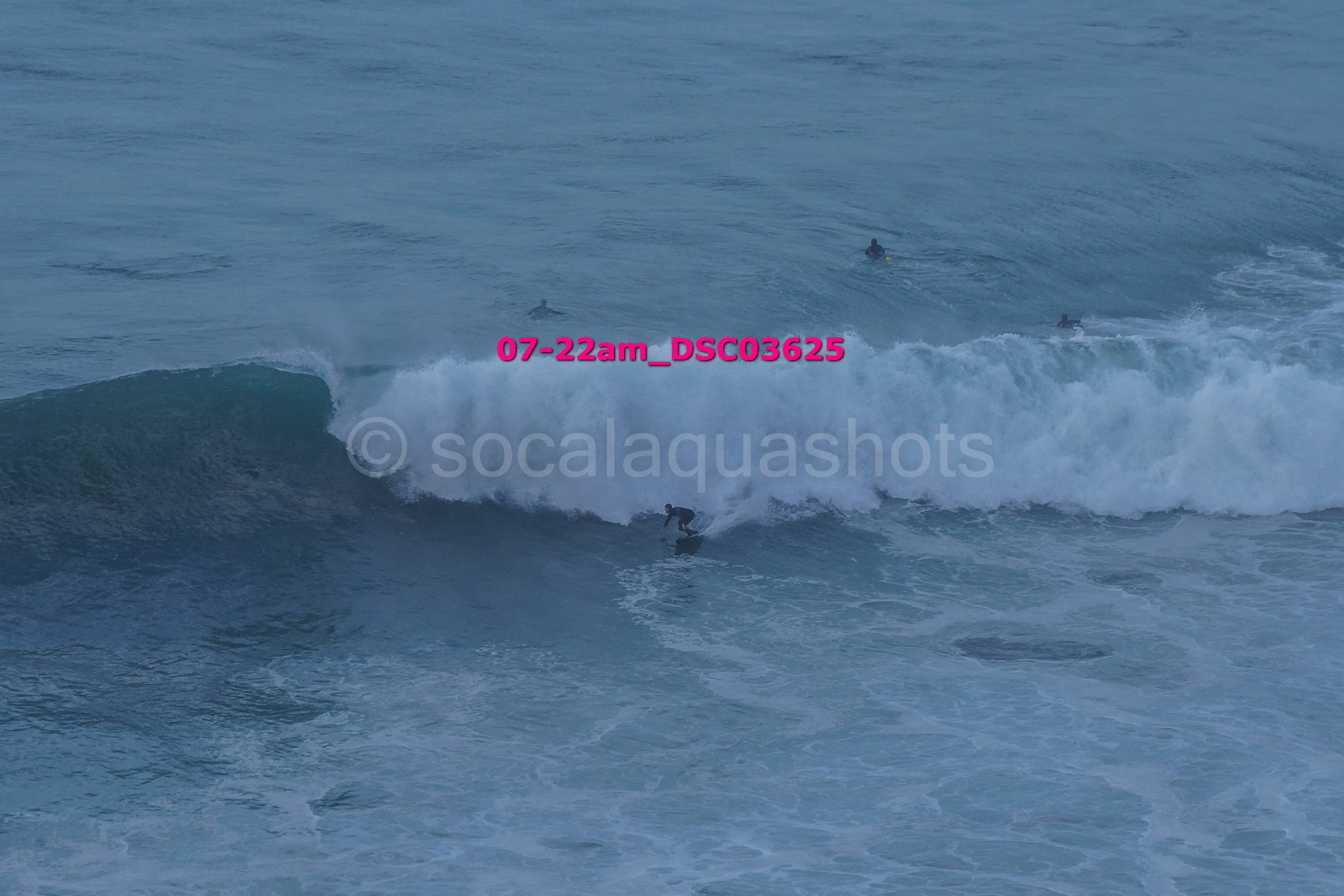 A person surfing on a wave with three surfers visible in the background in the ocean.