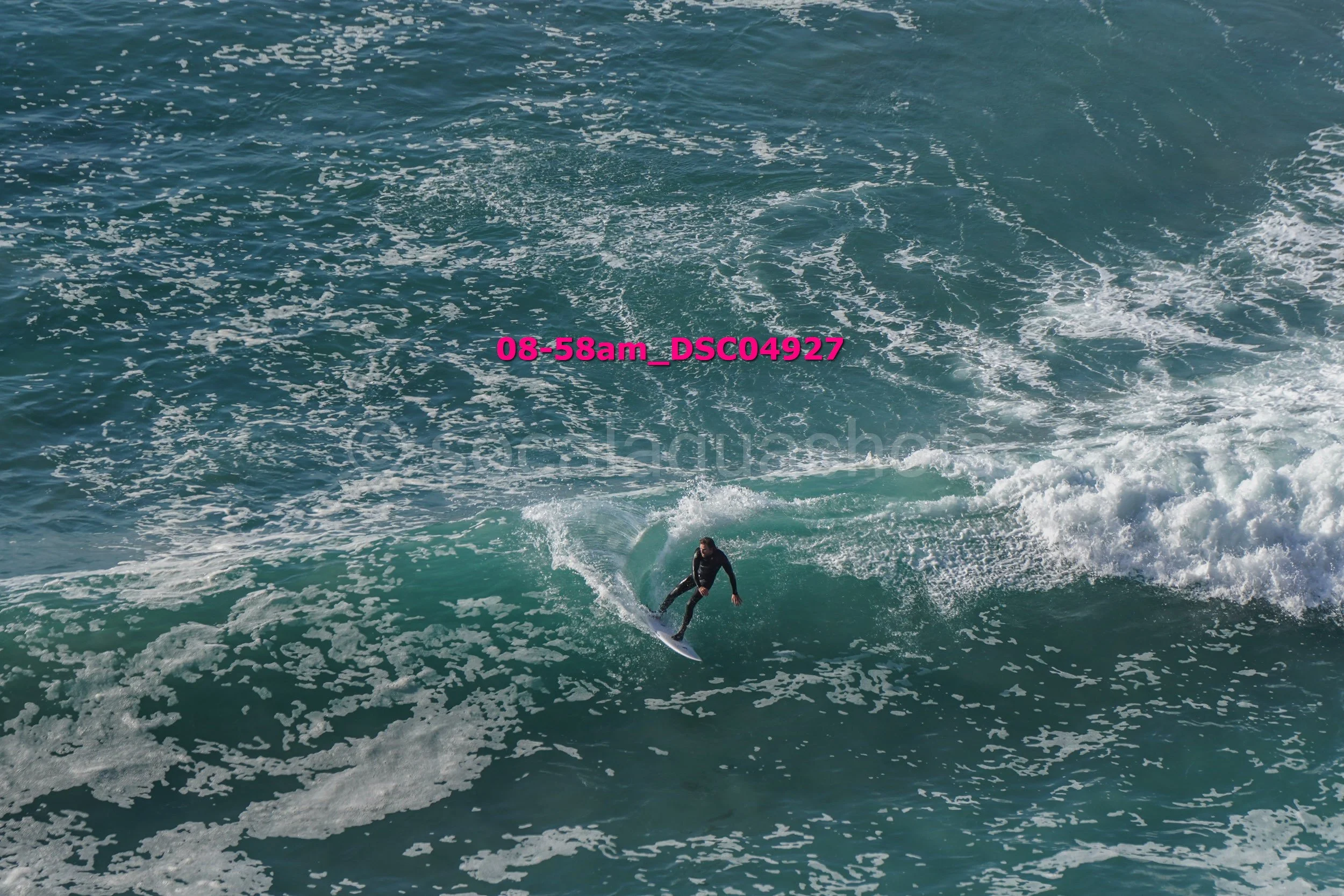 A person surfing on a wave in the ocean, with a time and location stamp overlayed that reads '08-58am_DSC04927'.